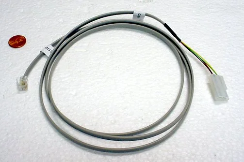 Electrical wiring cable with a gray outer insulation and connector at one end, lying on a white textured surface.