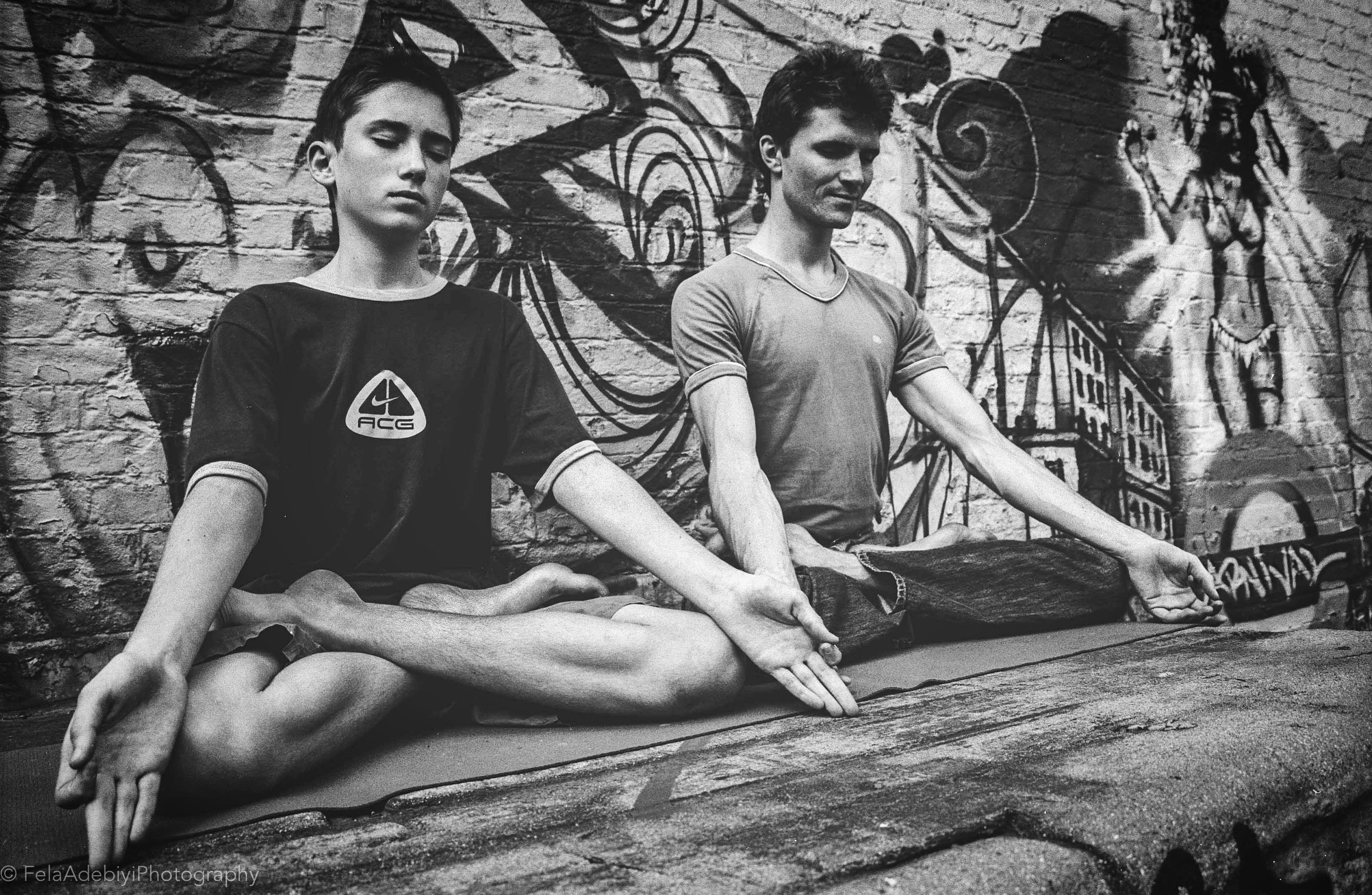 Two people meditating in lotus position against graffiti wall