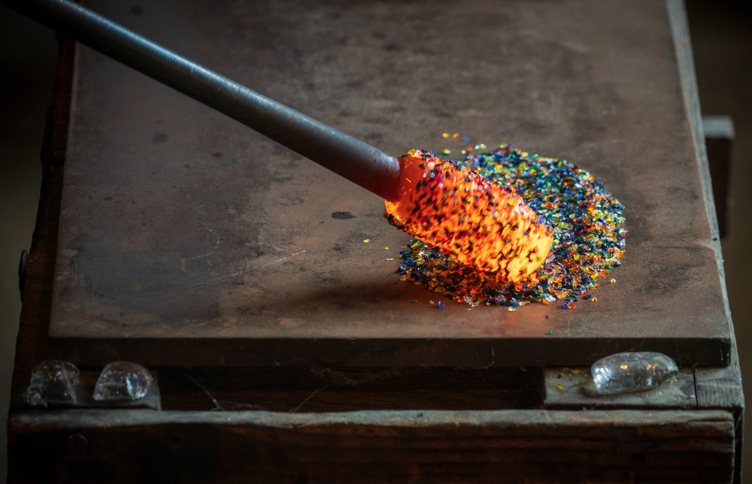 Glassblowing rod with molten glass and colored frit on table