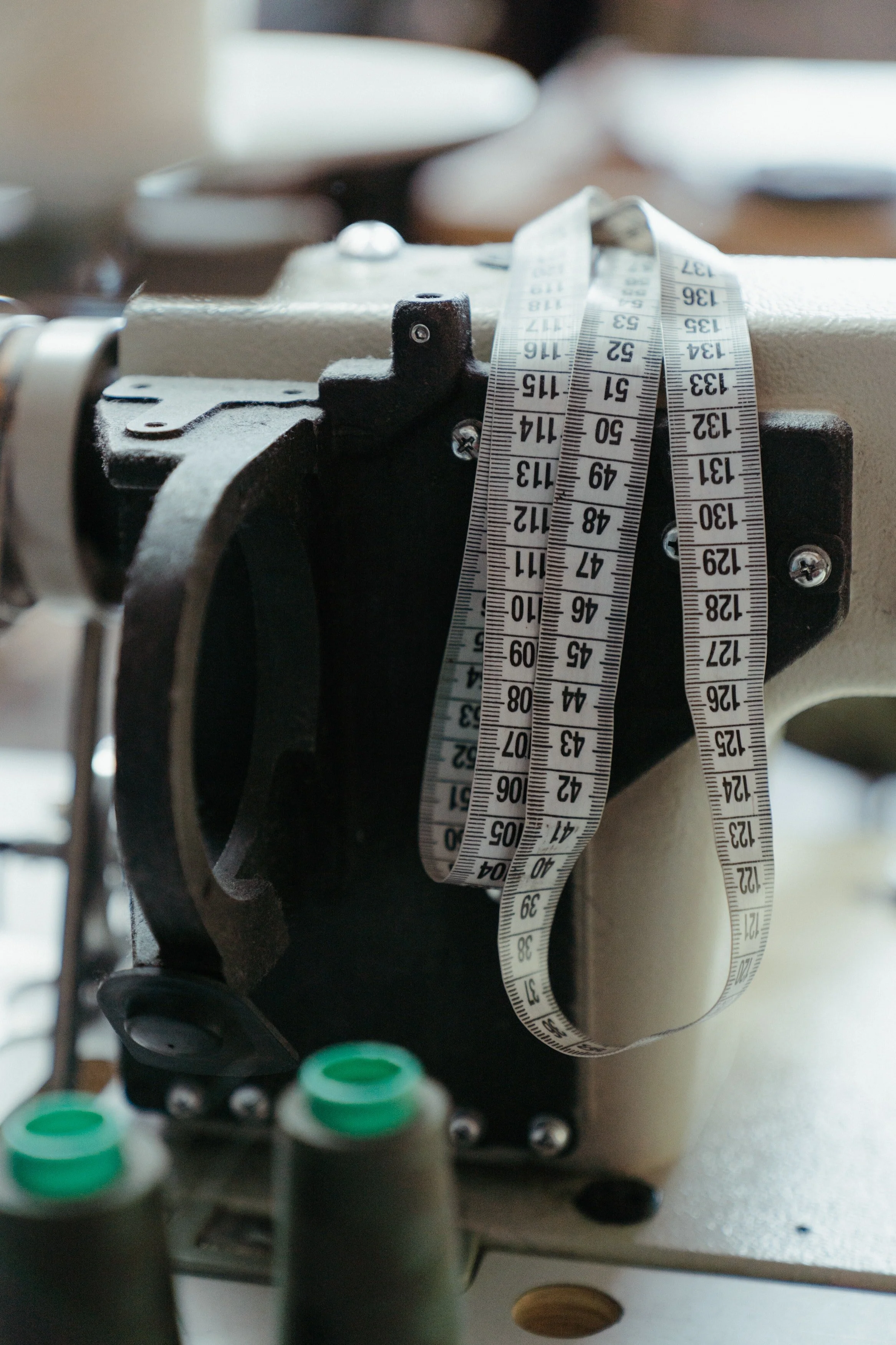 Close-up of a sewing machine with a measuring tape draped over it and green thread spools nearby.