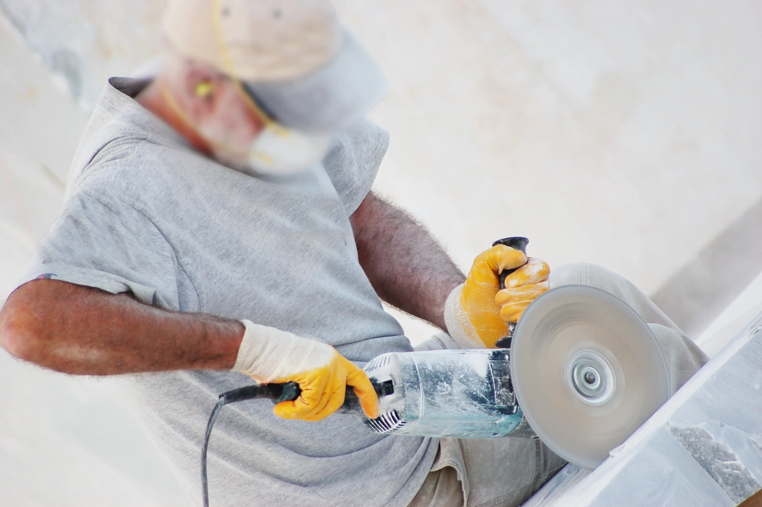 Person using an angle grinder to cut stone, wearing gloves and a protective mask.