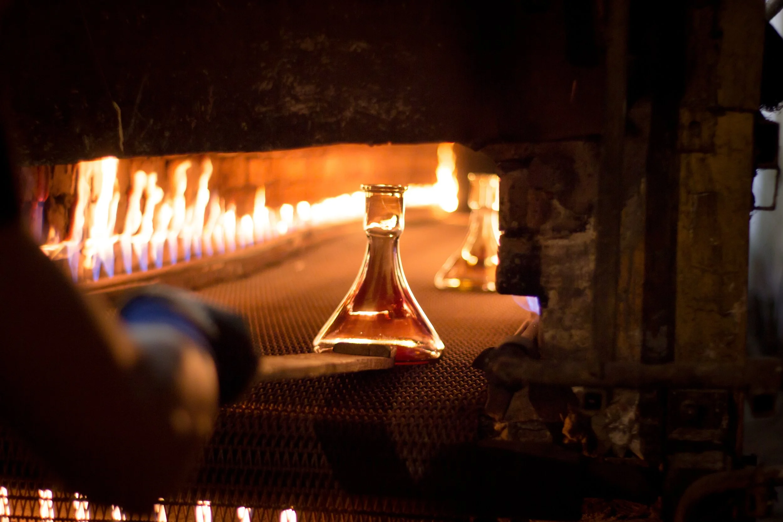 Glass flasks with brown liquid in a furnace, illuminated by flames.