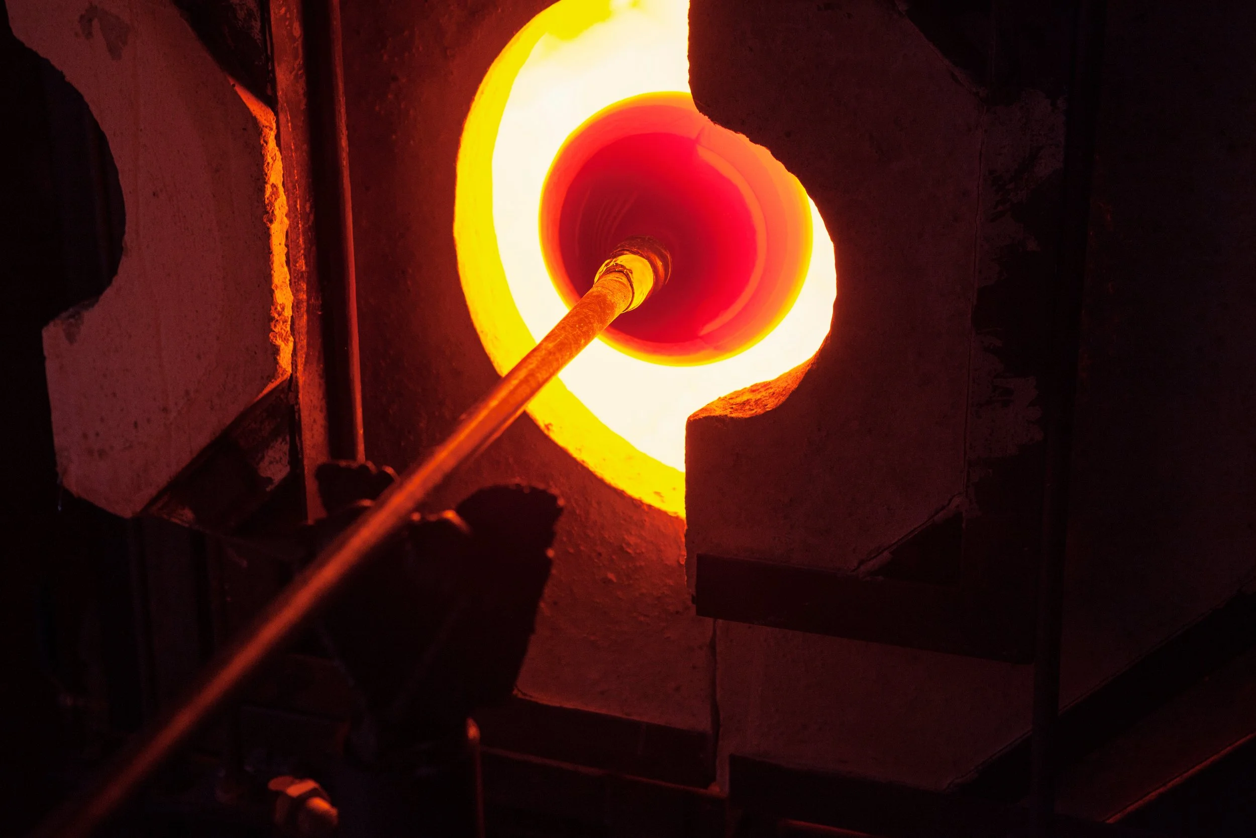 Glassblowing process in a hot furnace with molten glass on a rod.