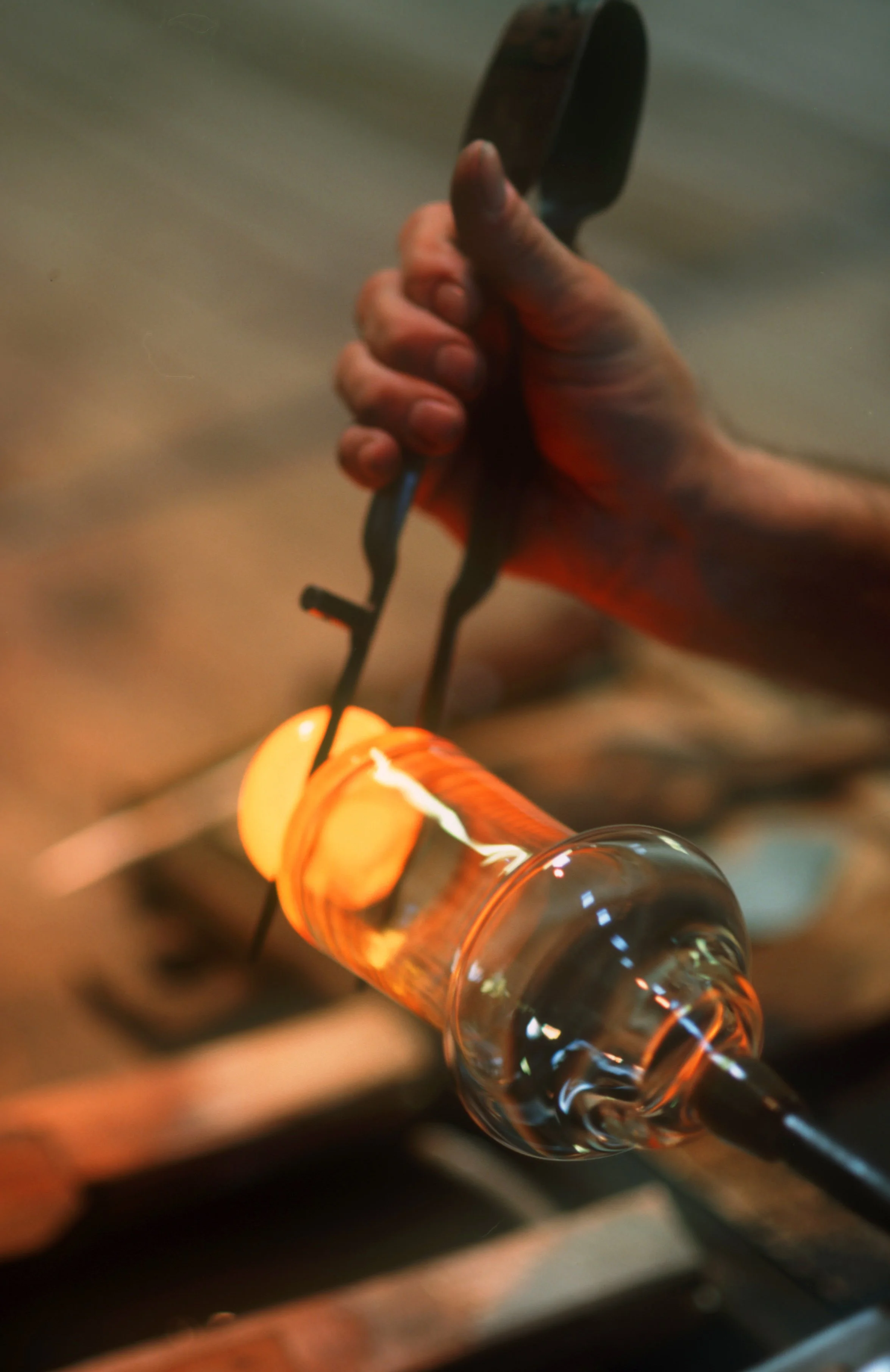 Close-up of a hand shaping hot glass with a tool in a glassblowing workshop.
