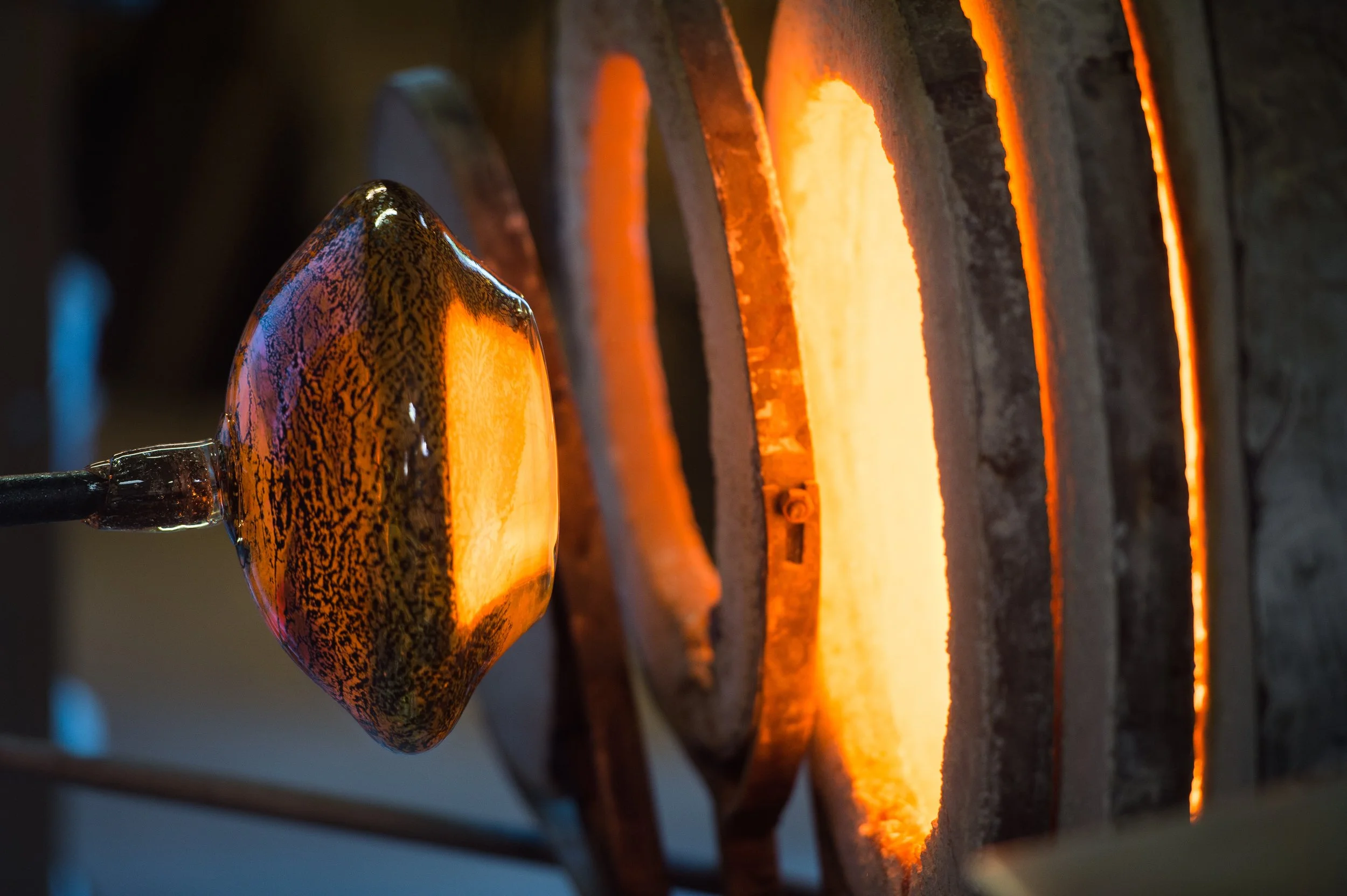 Molten glass on a rod being shaped near a furnace in a glassblowing studio.
