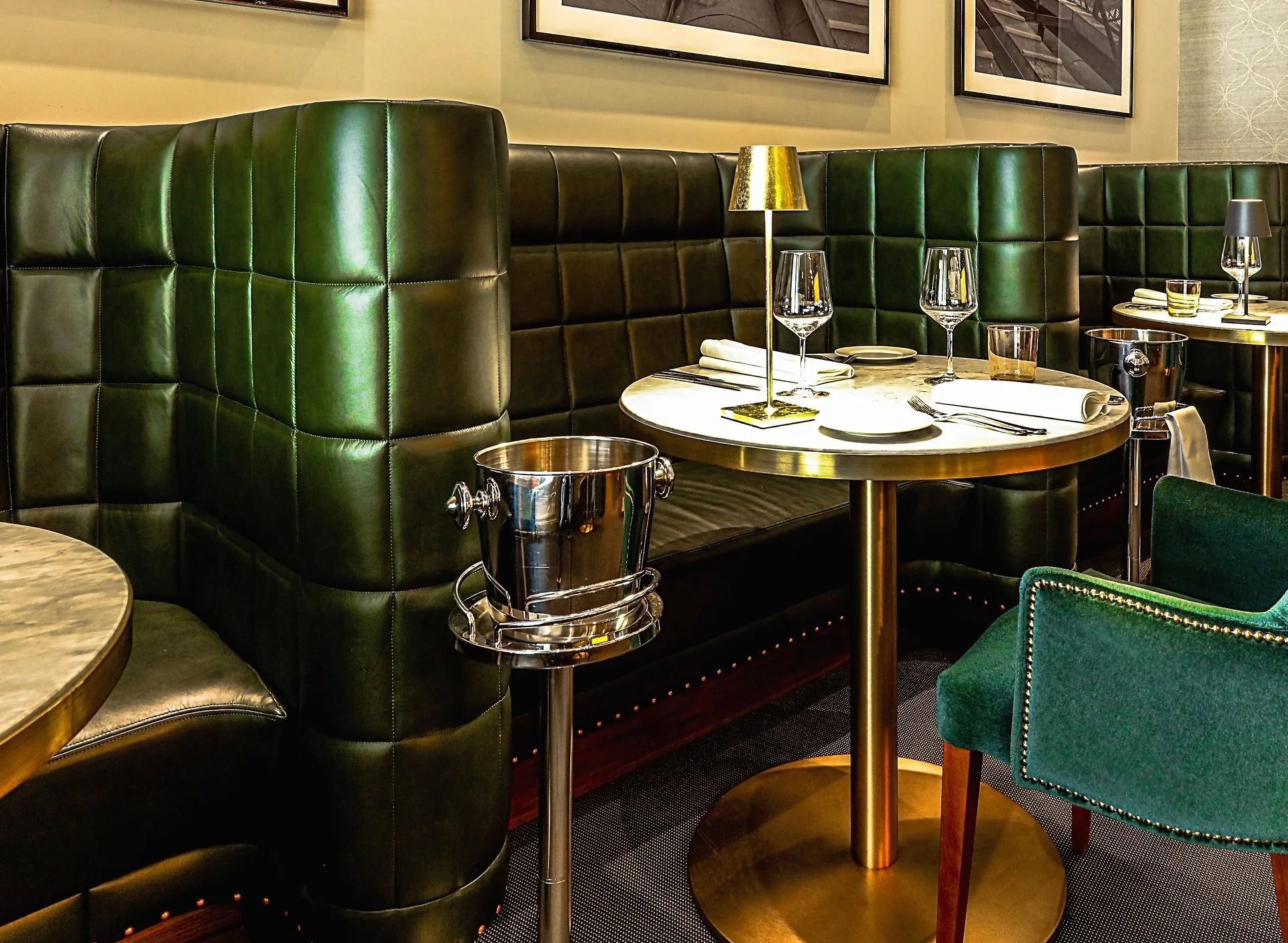 Elegant restaurant booth with green leather upholstery, gold-framed table, wine glasses, and a wine bucket stand.