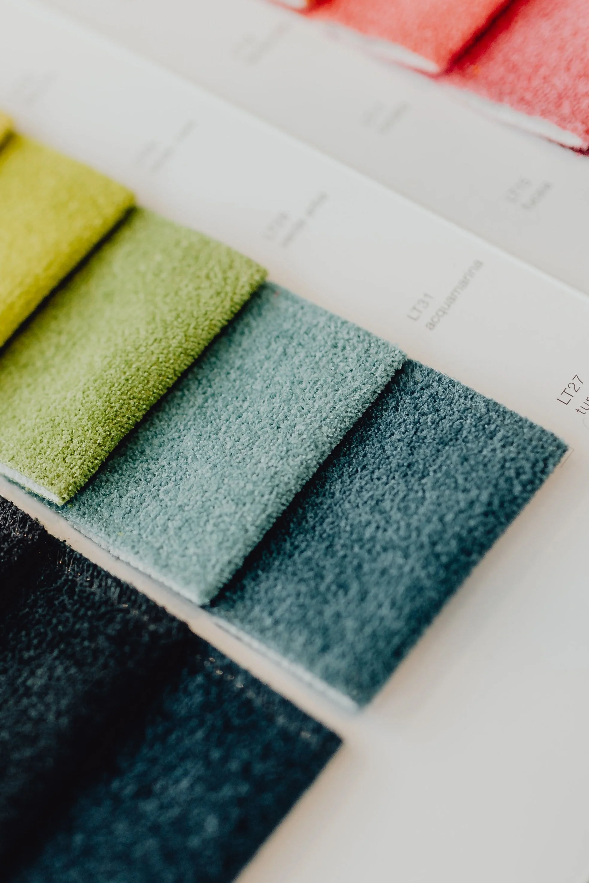 Close-up of colorful textile fabric samples in shades of green, blue, and gray arranged in a row on a catalog.
