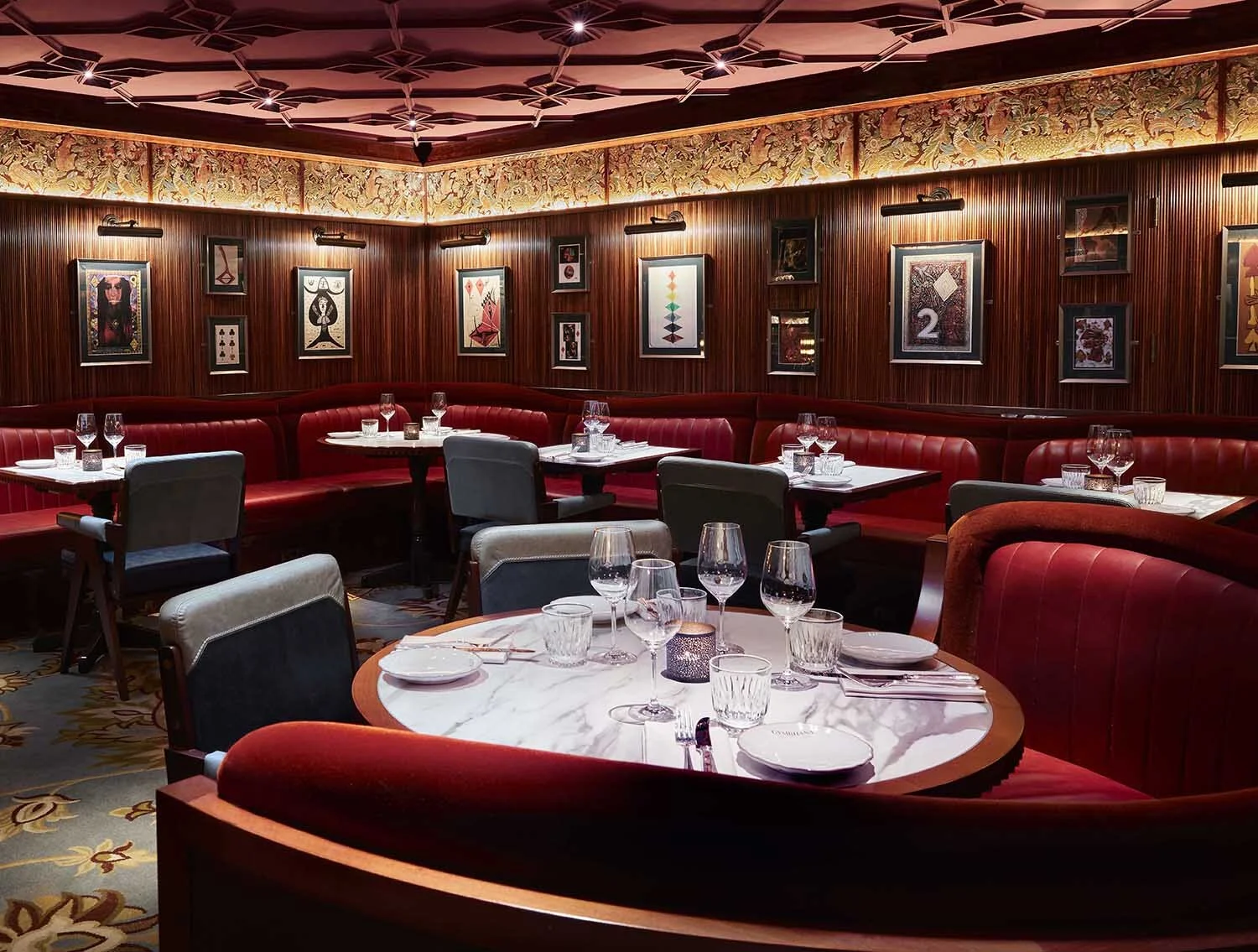 Elegant restaurant interior with red leather seating, marble tables, art-decorated walls, and dim lighting