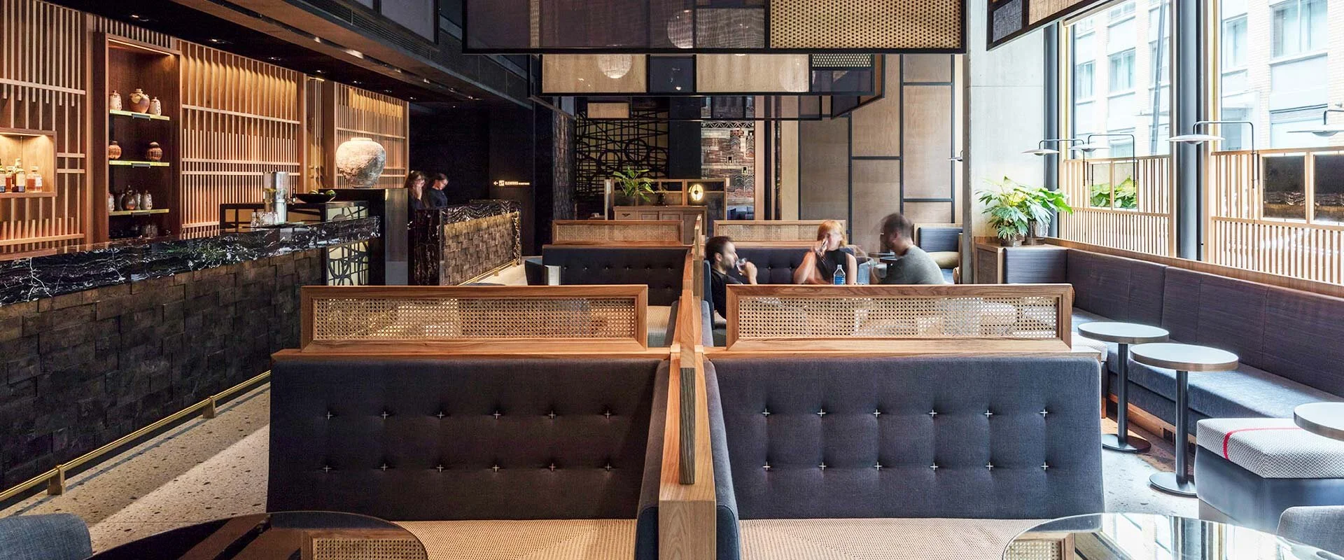 Modern restaurant interior with wooden booths and furniture, decorative wall shelves, and large windows.