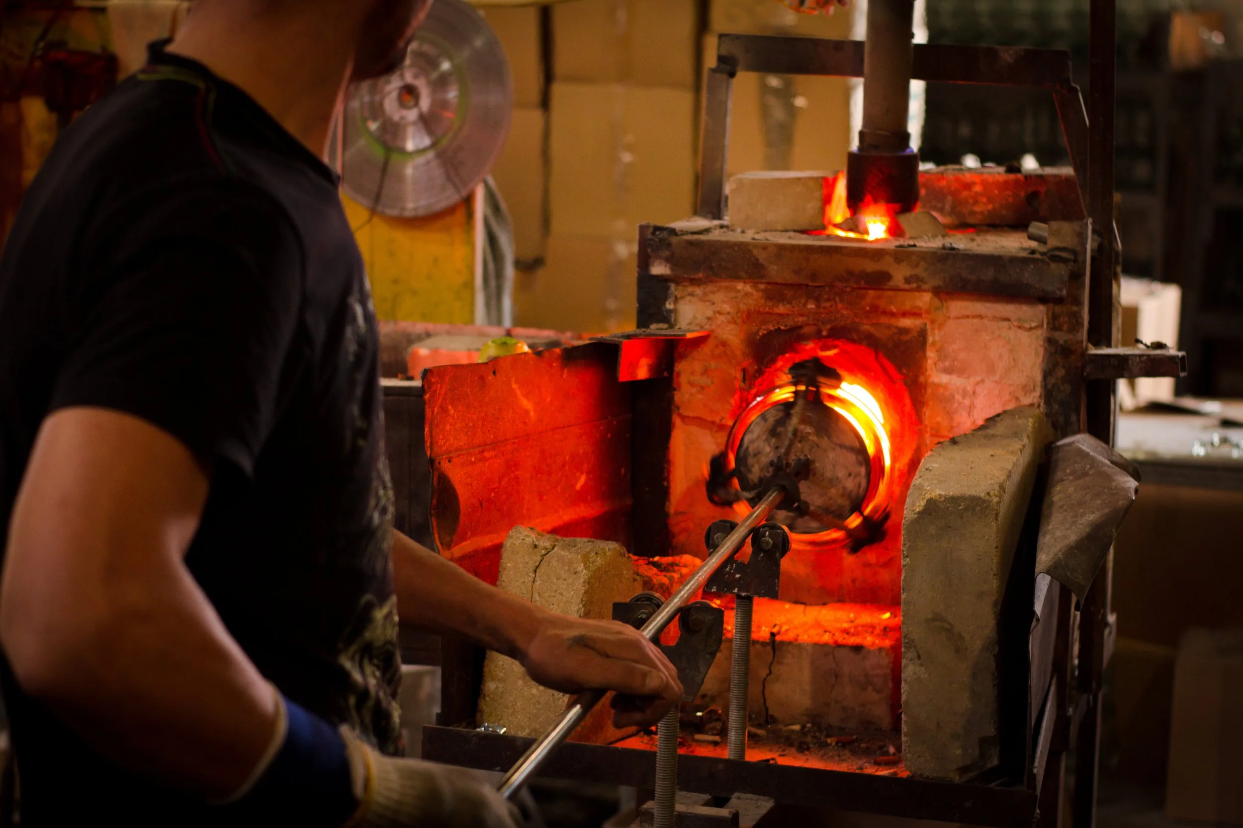 Person working with molten glass in a hot furnace