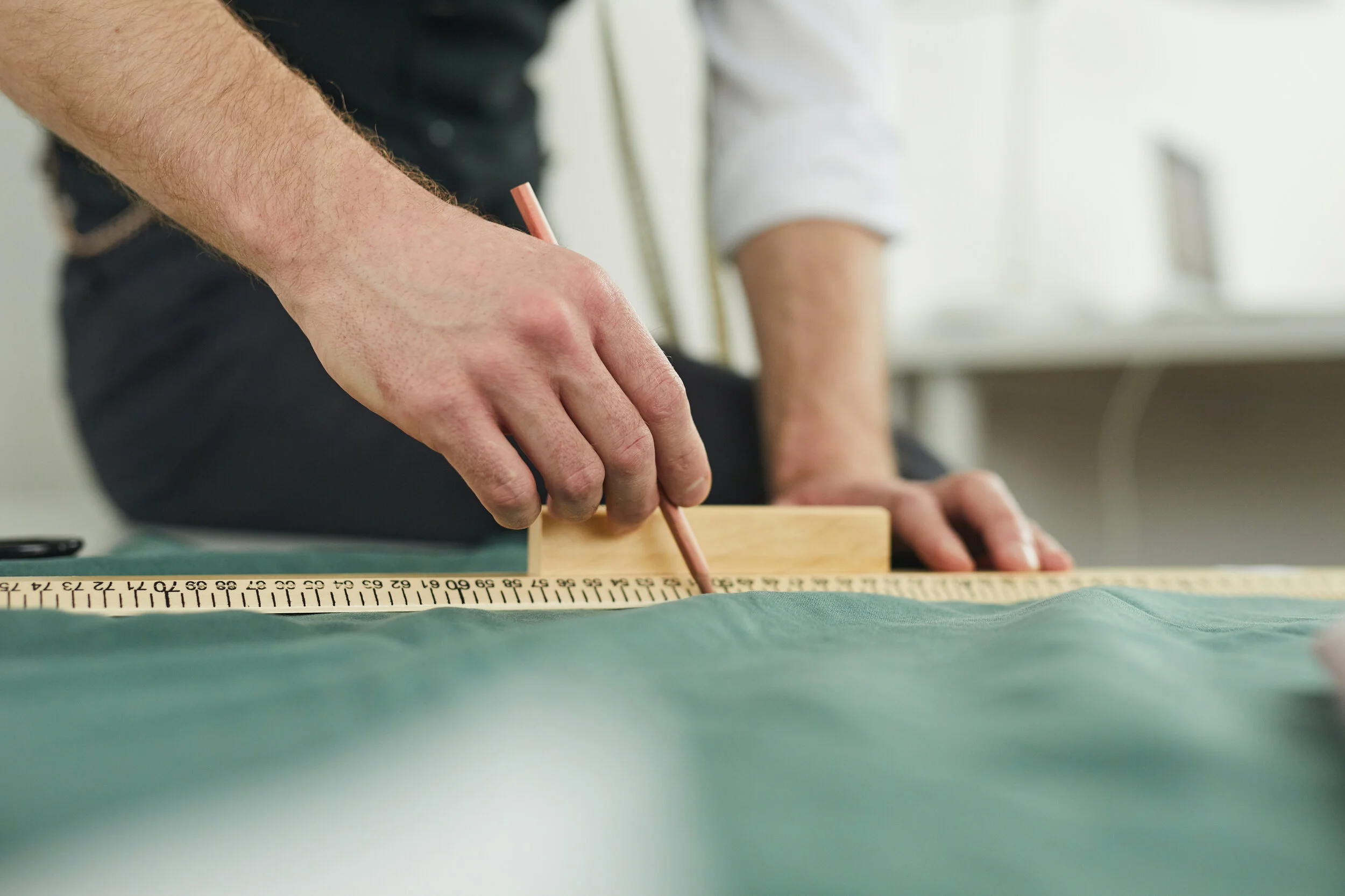 Tailor measuring and marking fabric with a pencil and ruler