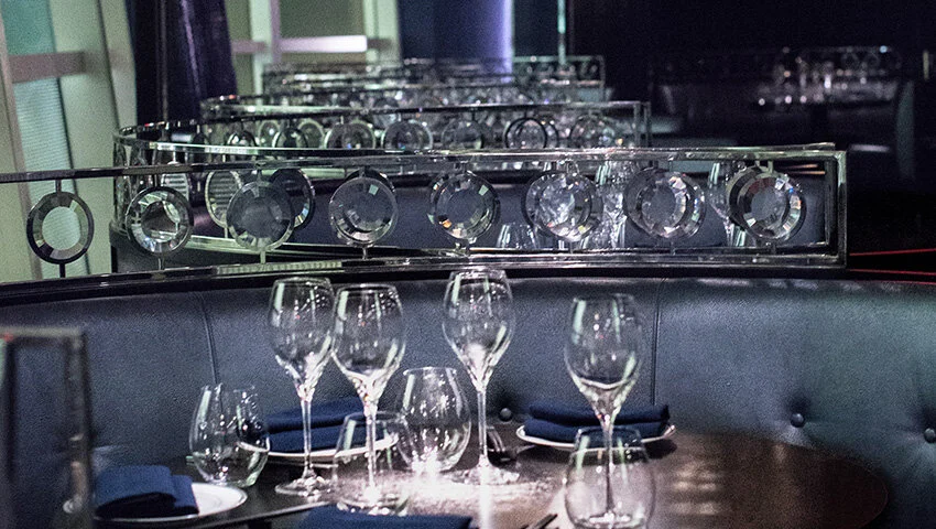 Elegant restaurant table setting with wine glasses, crystal decorations, and blue napkins on a round table.