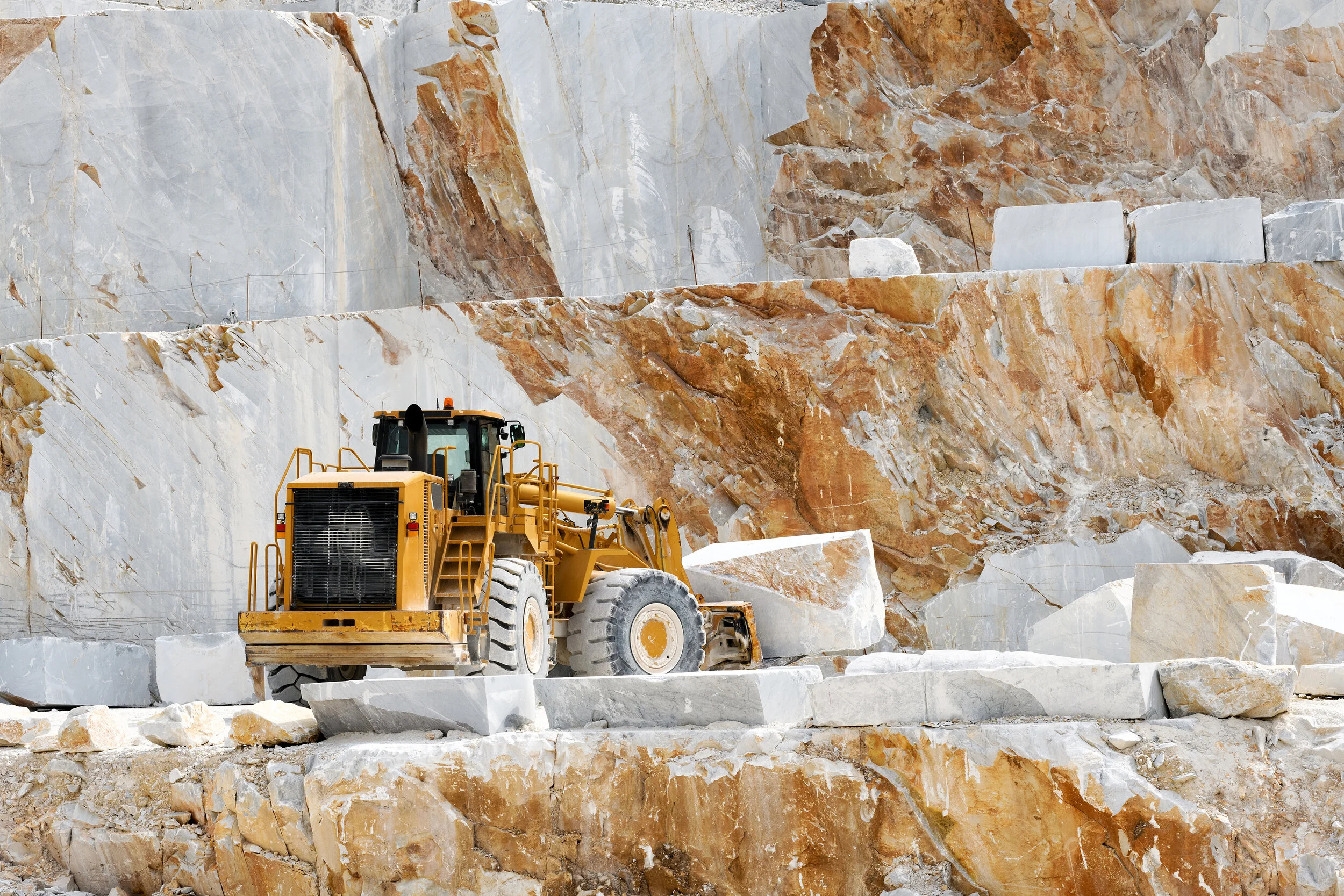 Yellow bulldozer in marble quarry with large stone blocks and rugged rock faces.