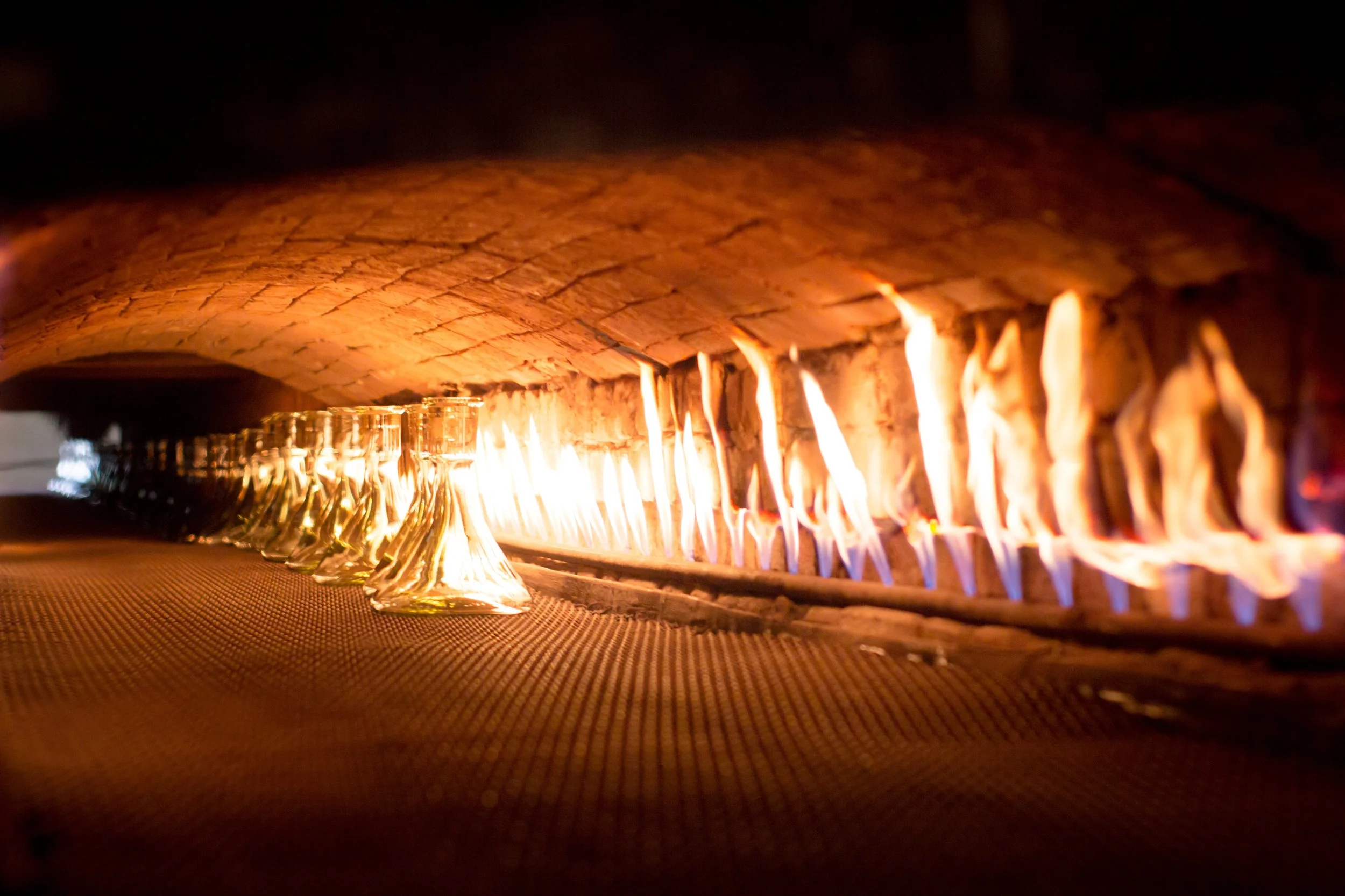 Glass bottles being heated in a furnace with flames inside a factory.