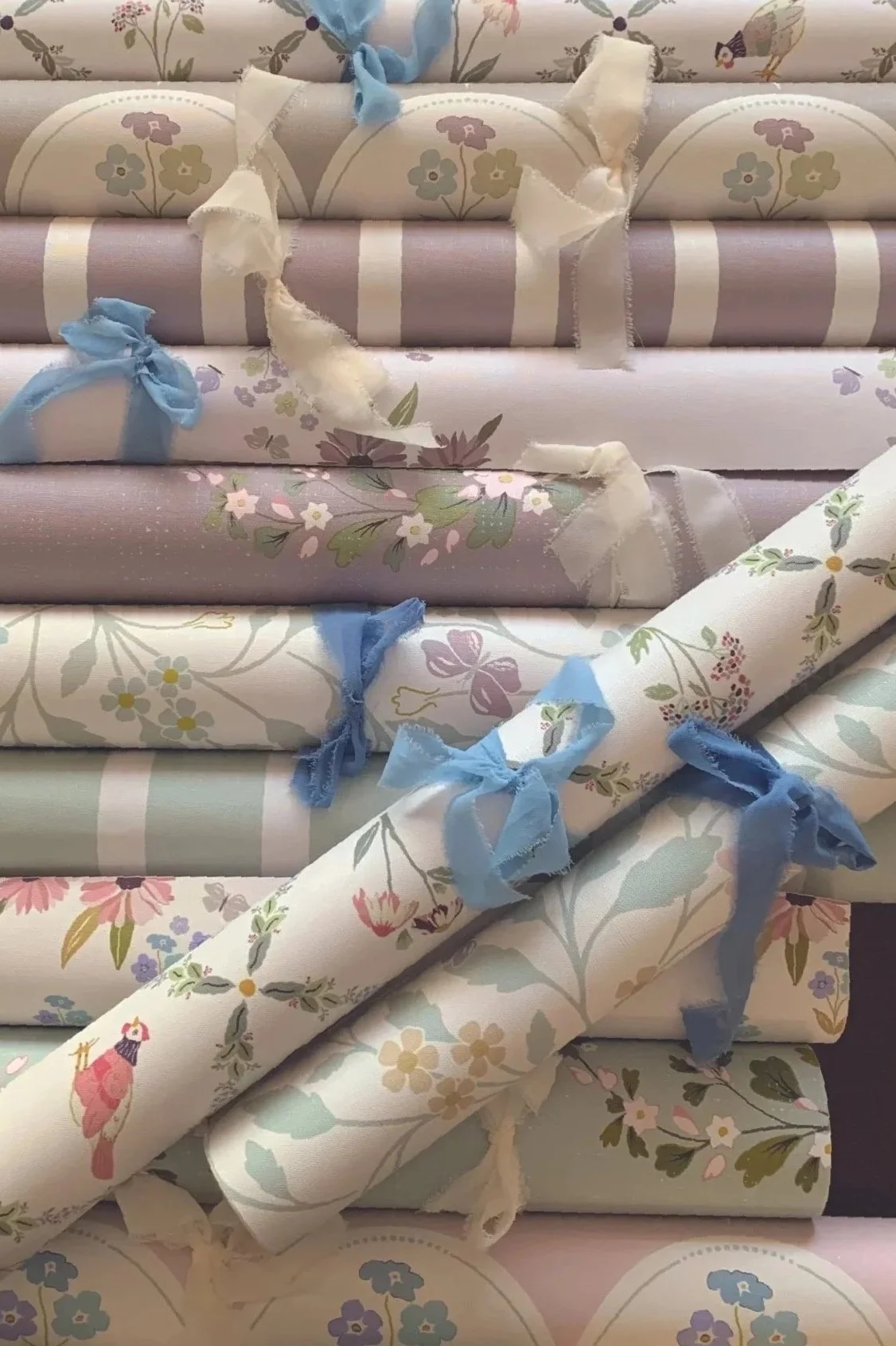Several rolls of decorative wallpaper with floral and animal patterns, tied with blue and white ribbons, arranged on a dark surface.