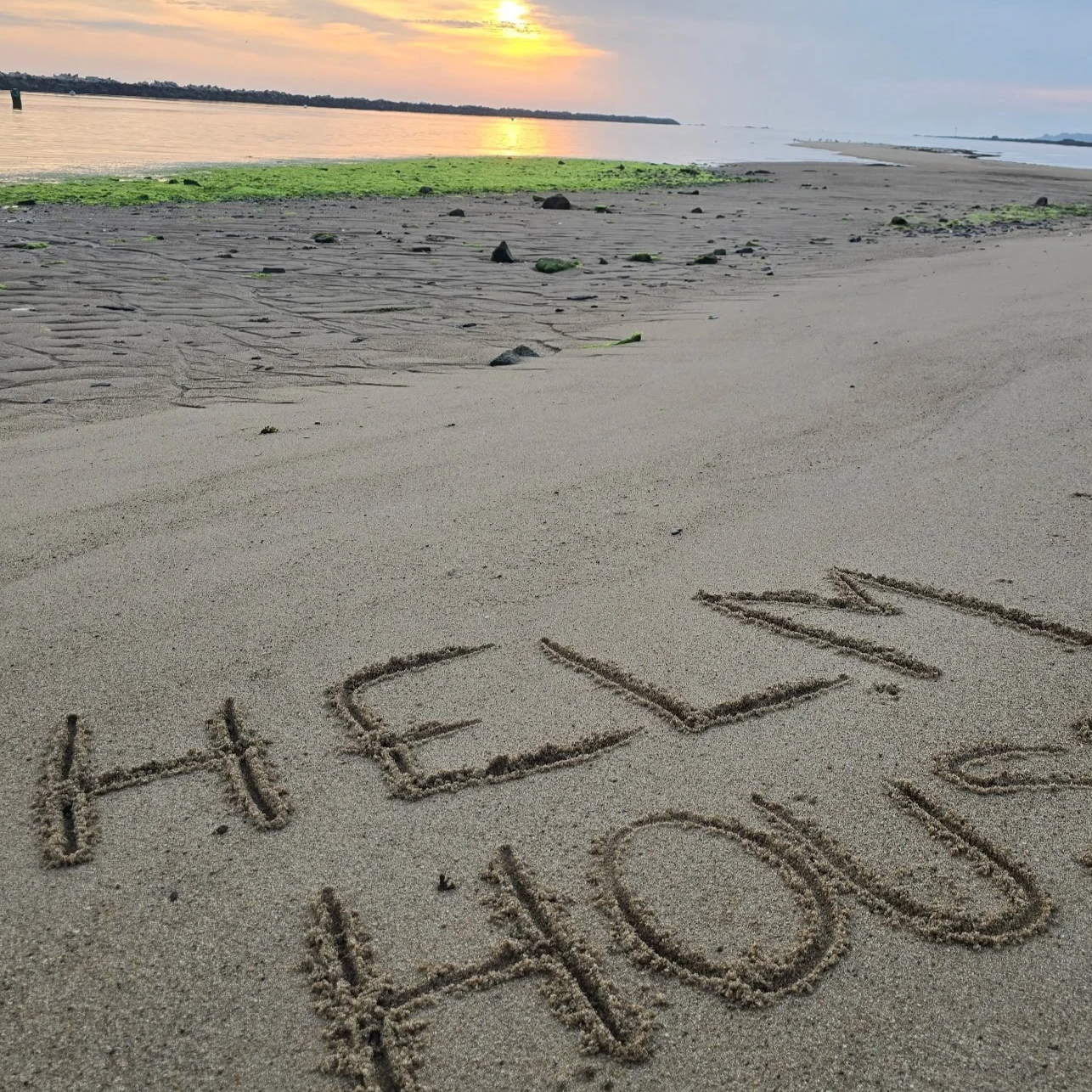 A beach at sunset with the words 'HELLO YOU' written in the sand in the foreground.
