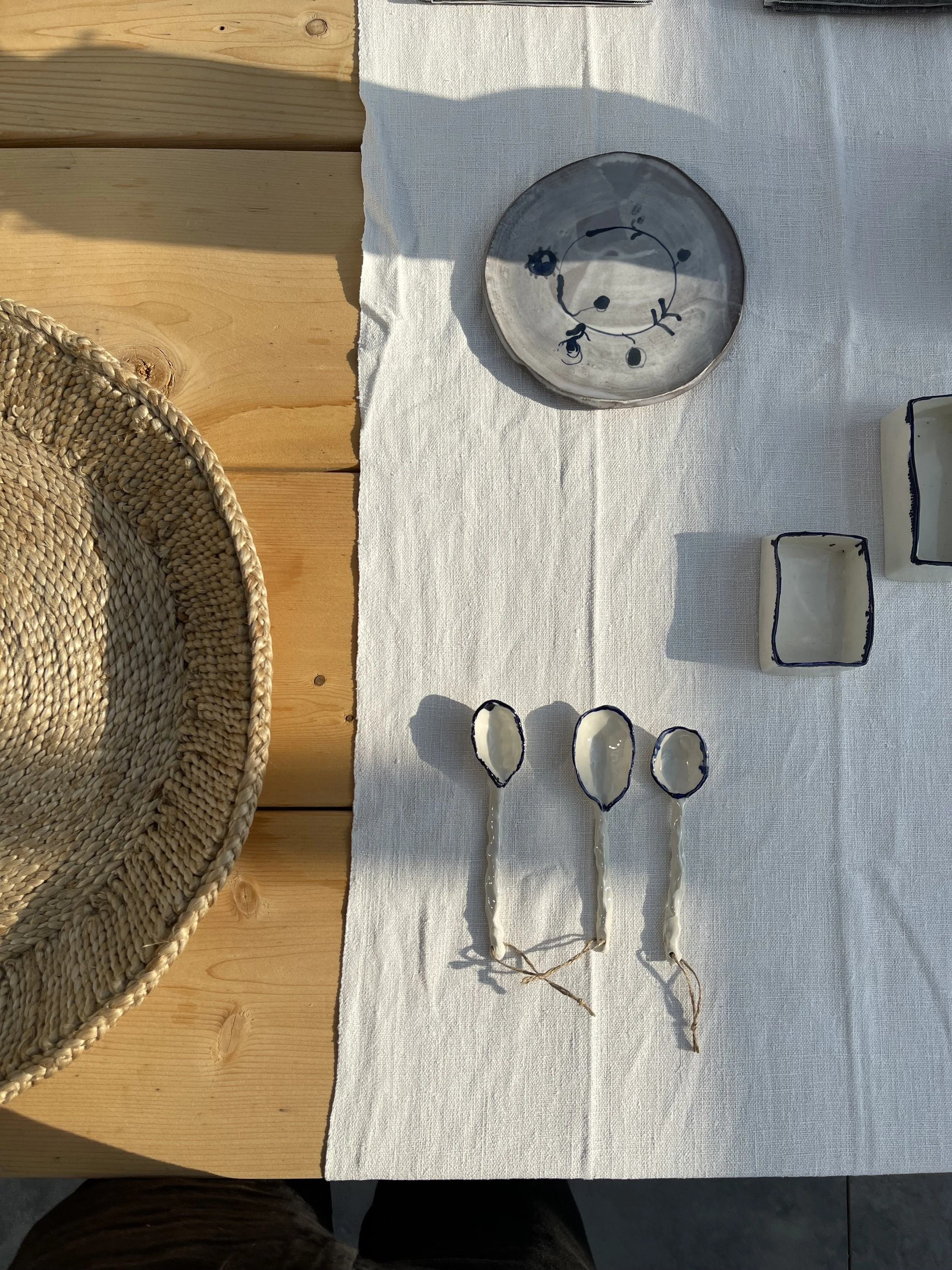 A white tablecloth with a ceramic bowl featuring a blue abstract design, and three white spoons with blue accents, all placed on a light wooden surface.