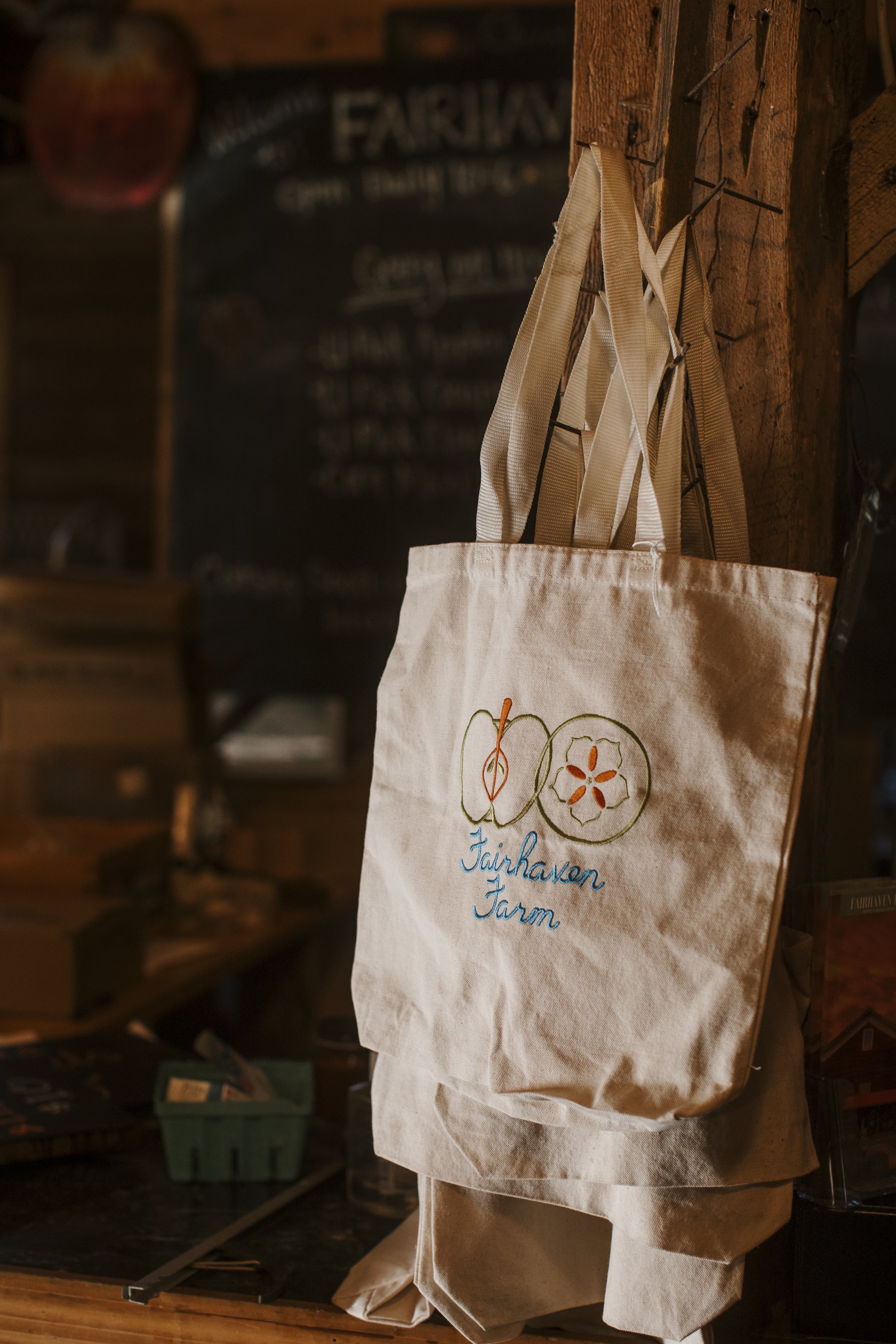 A canvas tote bag hanging on a wooden wall, embroidered with a logo and the words 'Taikhaven Farm' in blue script