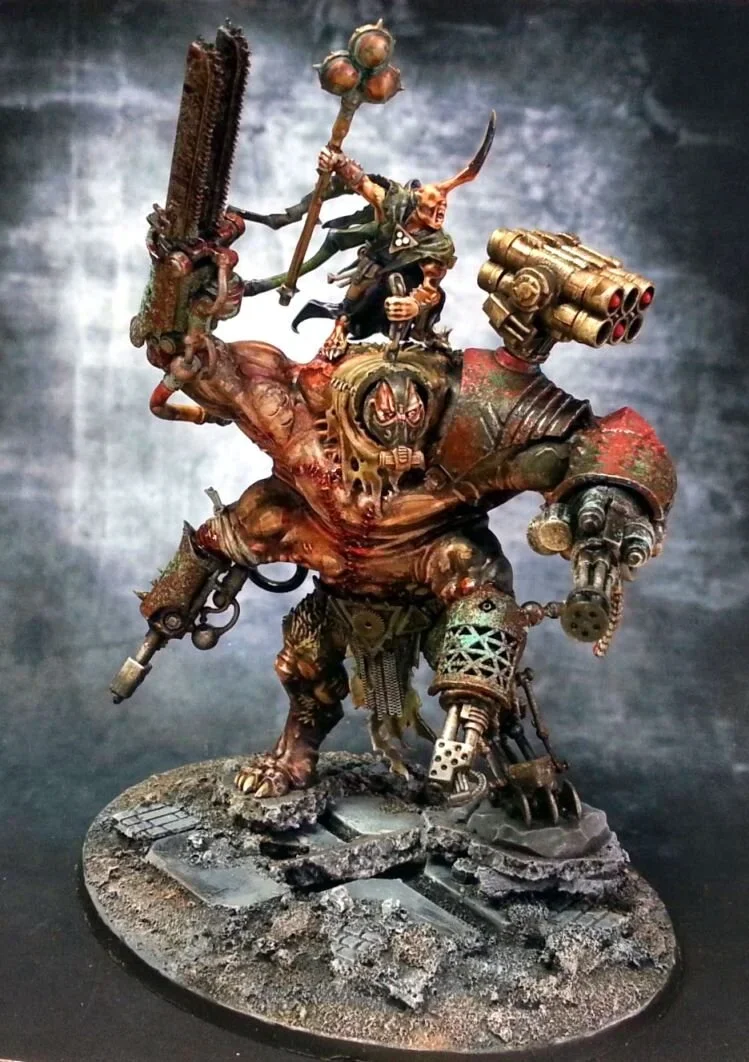 A detailed miniature figure of a large, grotesque creature with a skeletal face, robotic elements, and dystopian armor, holding a gun and a staff topped with a skull, set on a textured base resembling cracked earth.