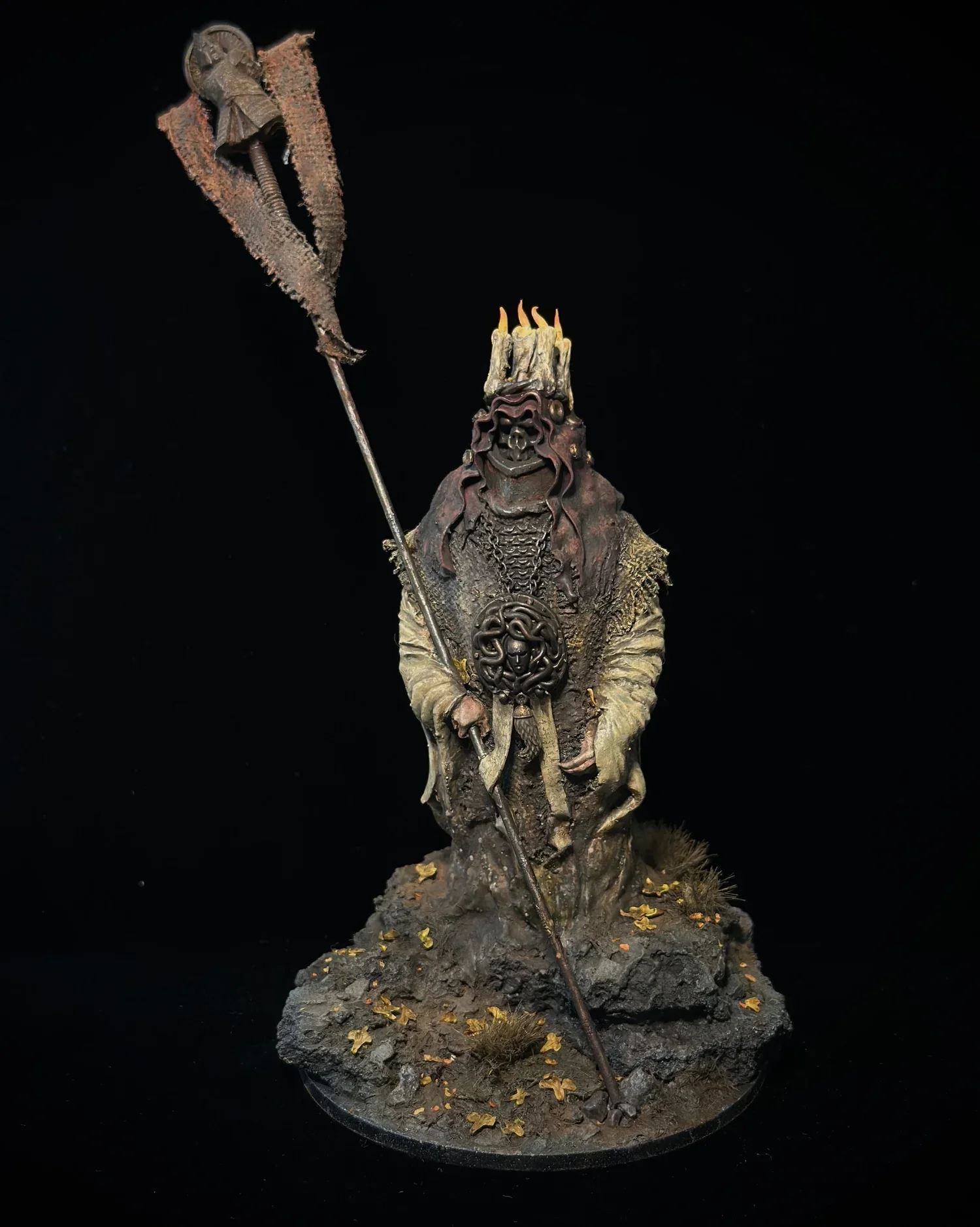 A detailed painted miniature of a fantasy witch or wizard character with a staff and skull decoration, standing on a textured base with fallen leaves.
