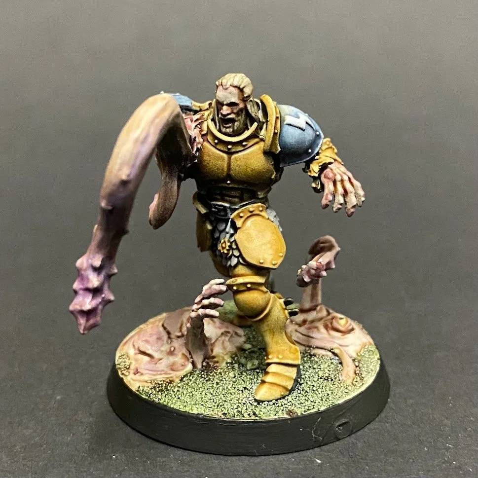 A detailed miniature figurine of a zombie in armor, running with a crazed expression, on a round base with textured ground and broken prosthetics.