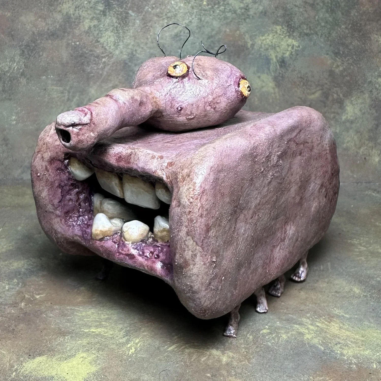 A surreal sculpture combining a pig's body with a large human mouth, having teeth and lips, and a pig's head with eyes and snout on top.