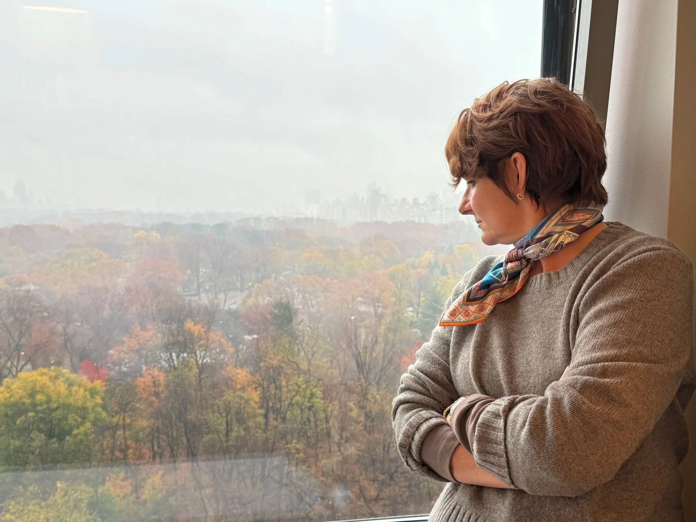 Jill Hoffman looking out a high window over a city in autumn