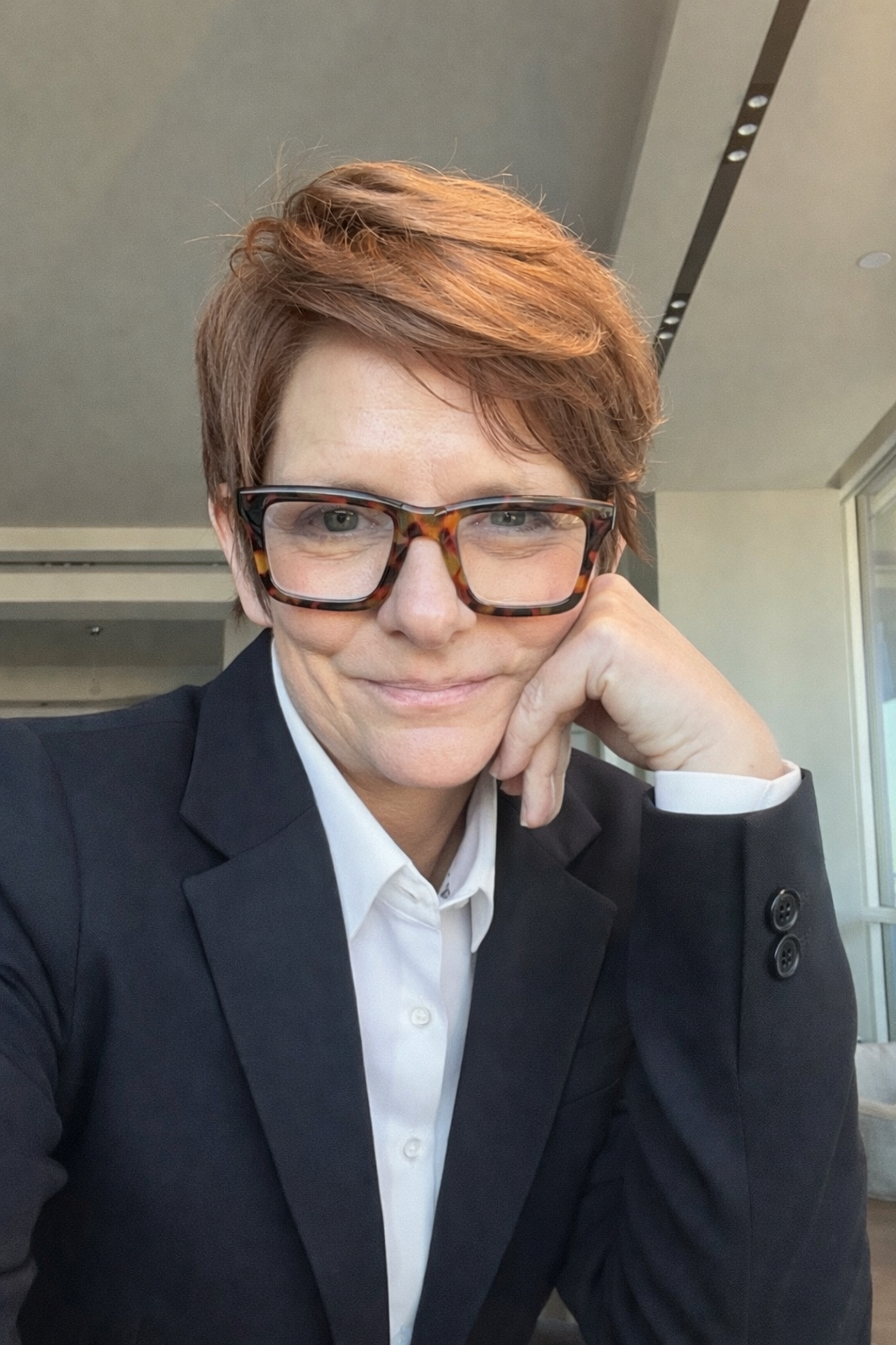 Jill Hoffman, writer and speaker, seated indoors and smiling, wearing a black blazer and white shirt.