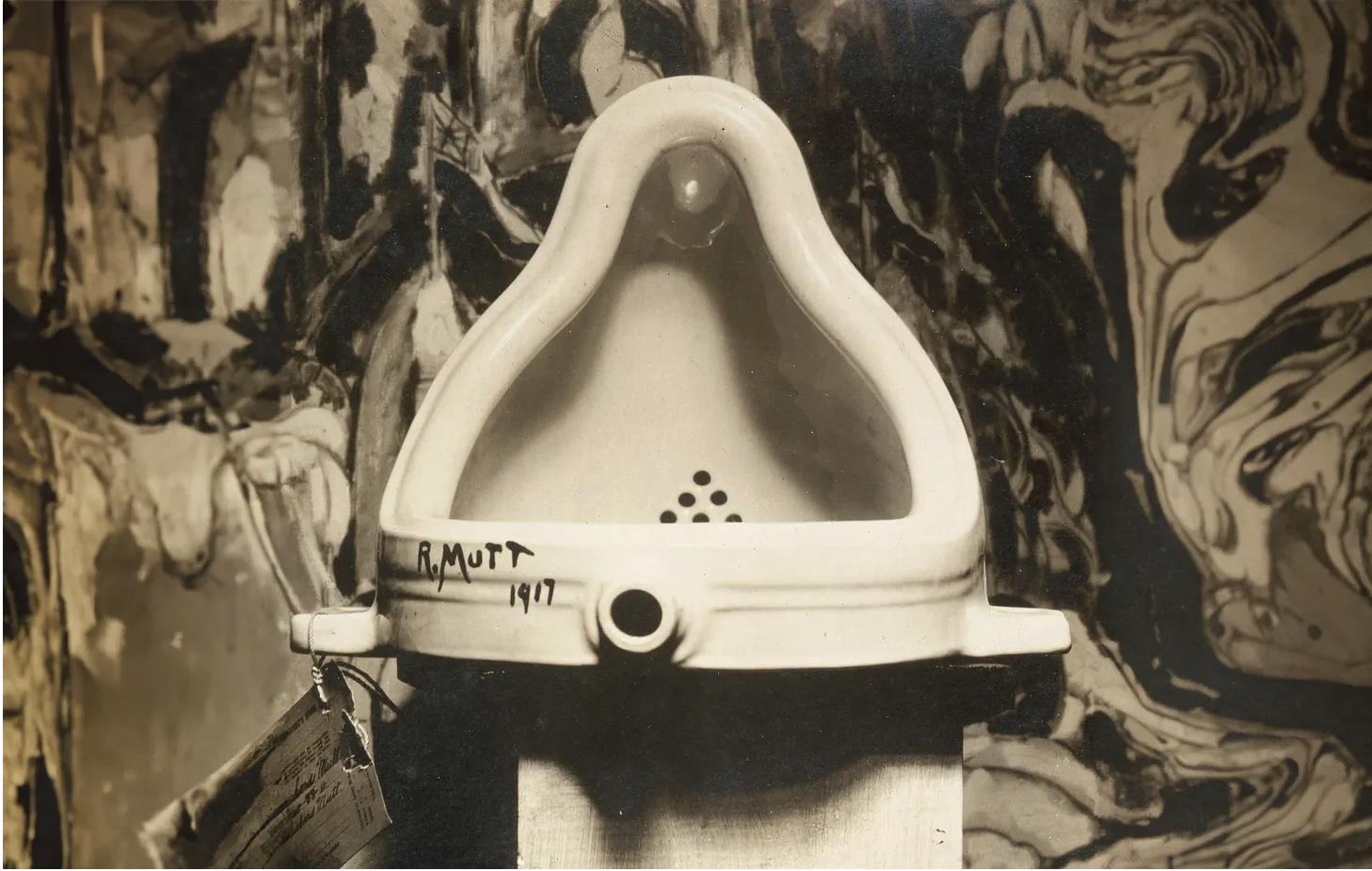 Alfred Stieglitz's 1917 photograph of Marcel Duchamp's Fountain: a white porcelain urinal signed R. Mutt 1917, on a pedestal in front of a painting