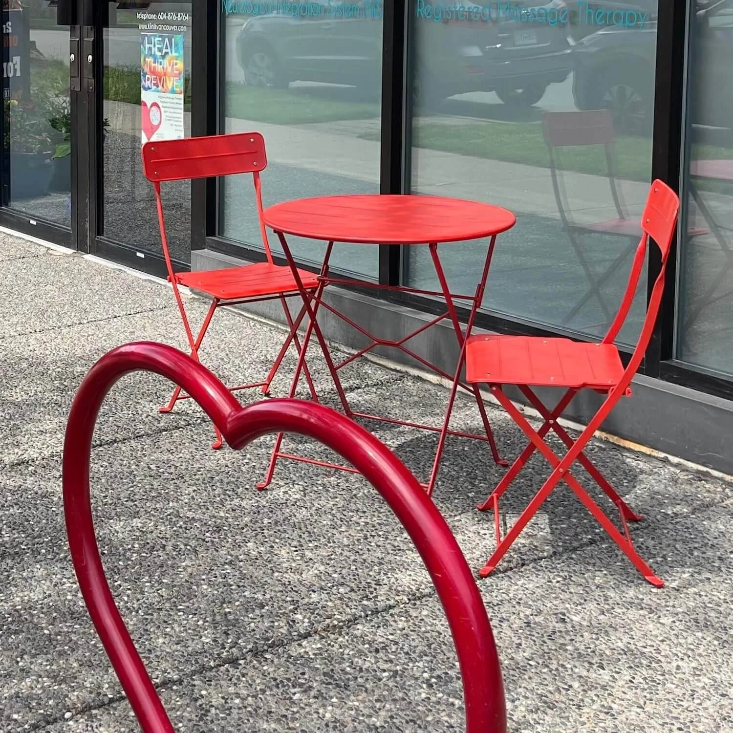Heart-shaped bike rack and red table and chairs out front of Klinik