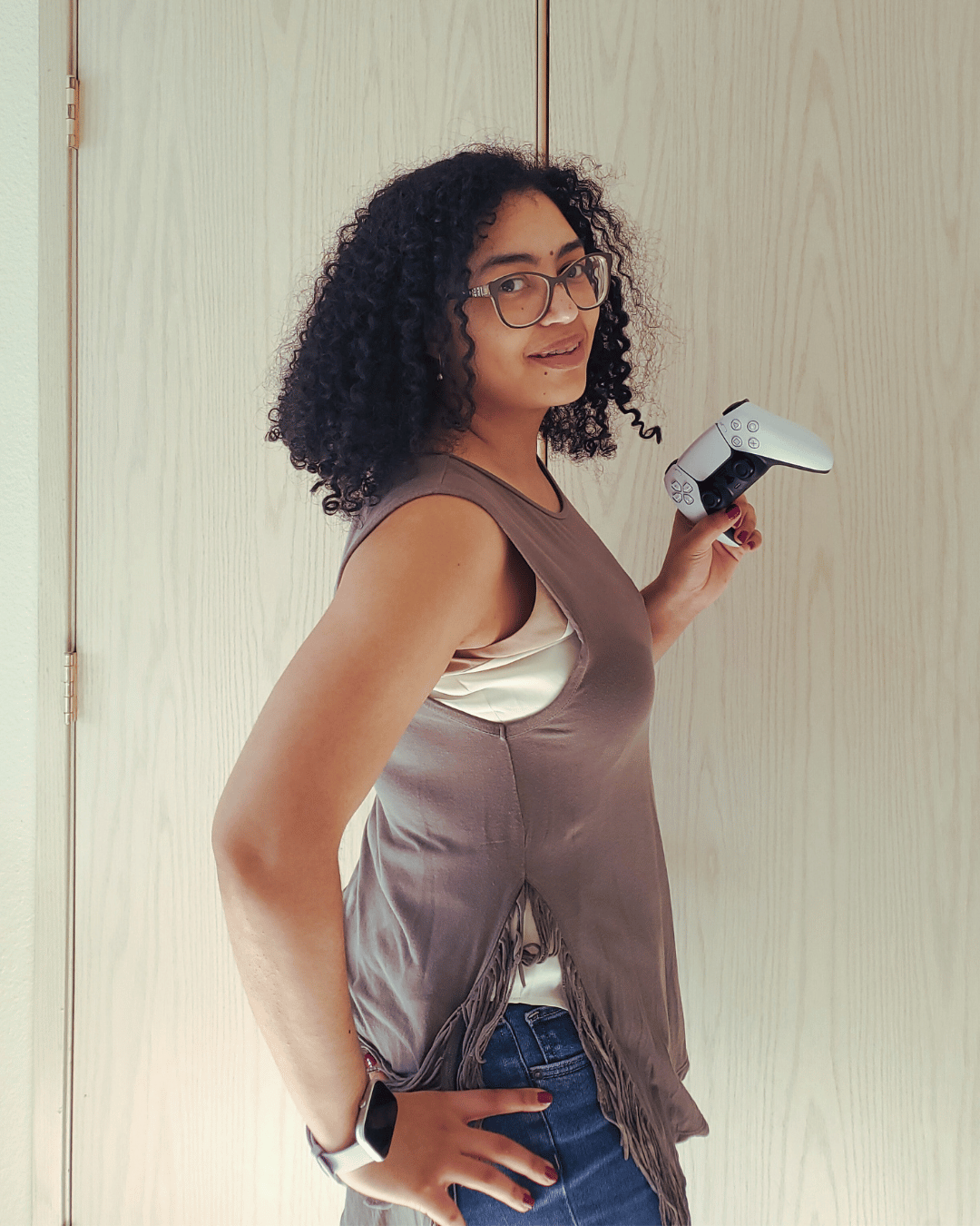 Smiling Isabelle standing sideways in an olive green muscle top, with one hand on her hip and the other holding up a white and black PlayStation 5 controller, symbolizing email funnels and the "choose-your-email-adventure" concept.