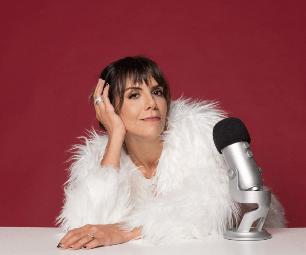 Marisa Corcoran, copy mentor and creator of The Copy Chat, wearing a white fur coat with her left hand resting on her head, next to a silver microphone.