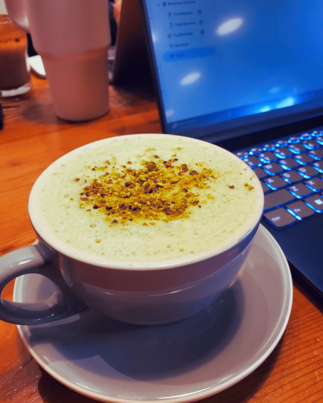 Matcha latte in a cafe mug with a laptop and pink water bottle on a coworking table.