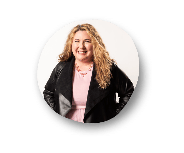 Jennifer Copper, TEDxSammamish Women Organizer and Founder of InWorthy is smiling and wearing a pink top, a black leather jacket, and a pink beaded necklace.