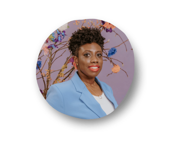 Yaa-Hemaa Obiri-Yeboah, Founder of The Y Variable, smiling in a baby blue blazer over a white top. She stands against a grayish-purple background adorned with colorful flowers and tree branches.
