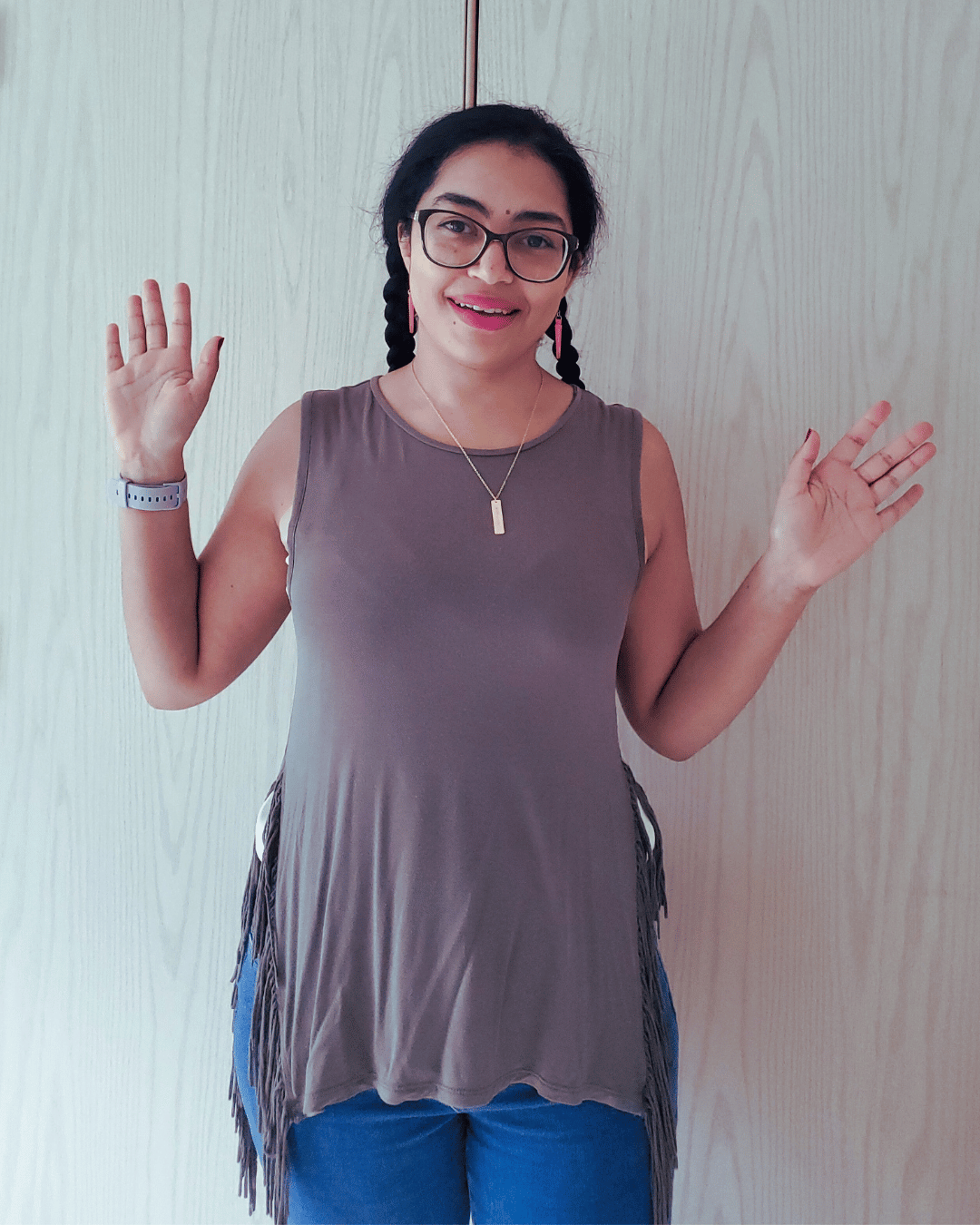 Smiling Isabelle waving with both hands up, wearing an olive green muscle top and a gold necklace.