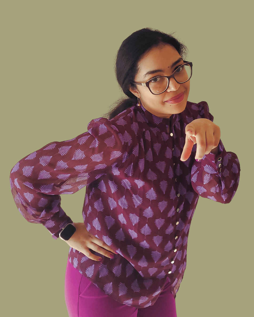 Isabelle Sarley, Email Marketer and Copywriter, smiling and wearing a purple blouse and suit pants, leaning towards the camera with one hand on her hip and the other pointing towards you.