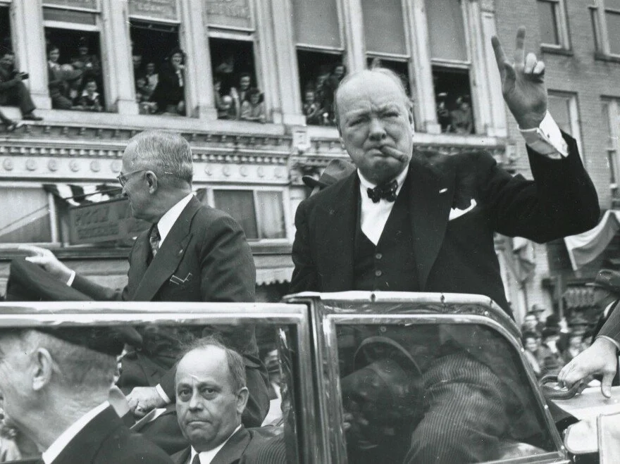 Sir Winston Churchill is seen doing the peace sign to a crowd as he rides in a motorcade.