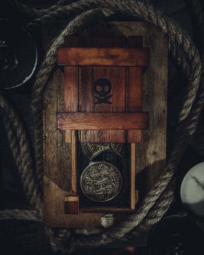 A wooden box with a skull and crossbones symbol on it, containing pirate coins, surrounded by ropes and candles.