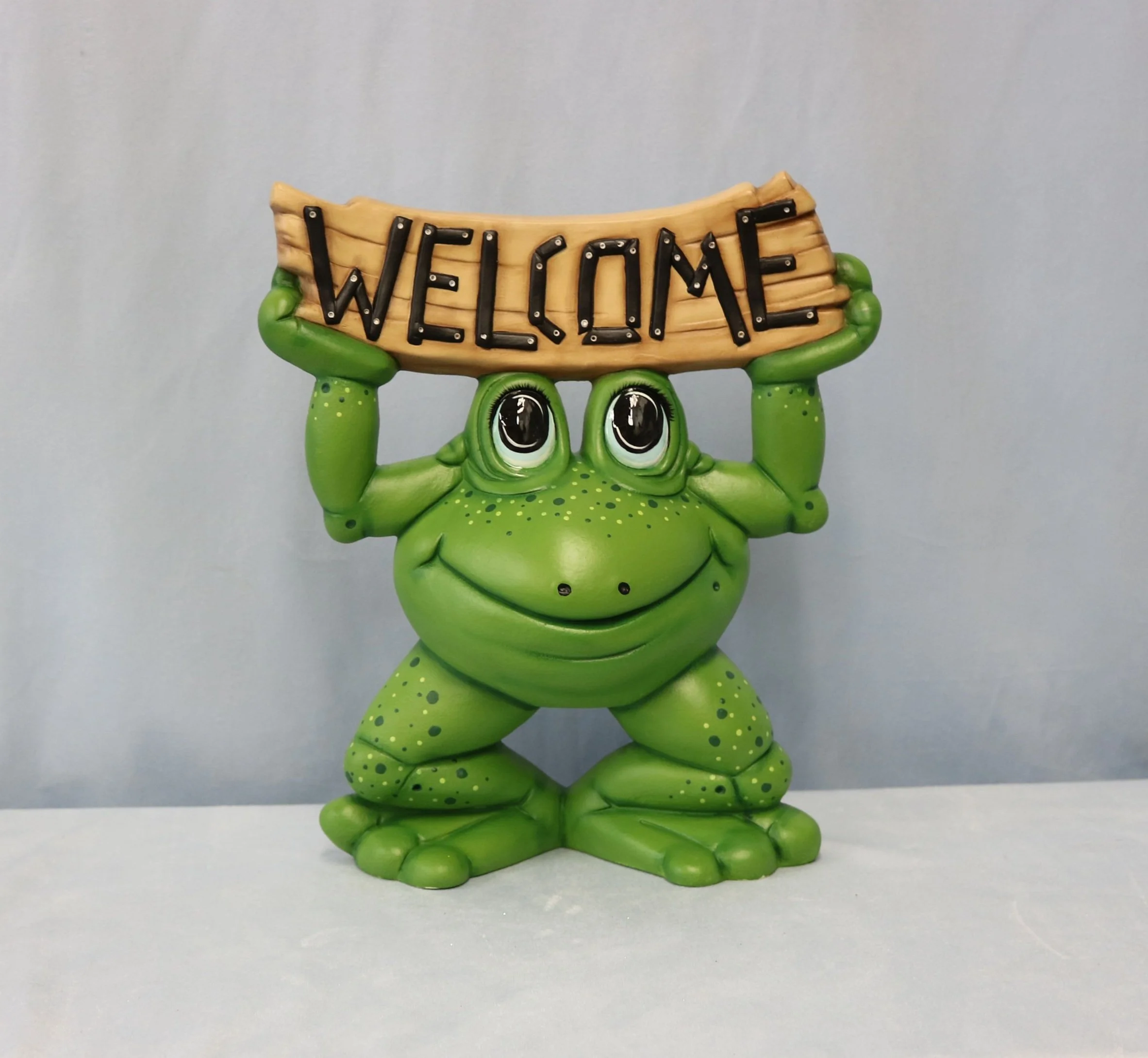 A green  frog holding a sign that reads "Welcome" in black letters.