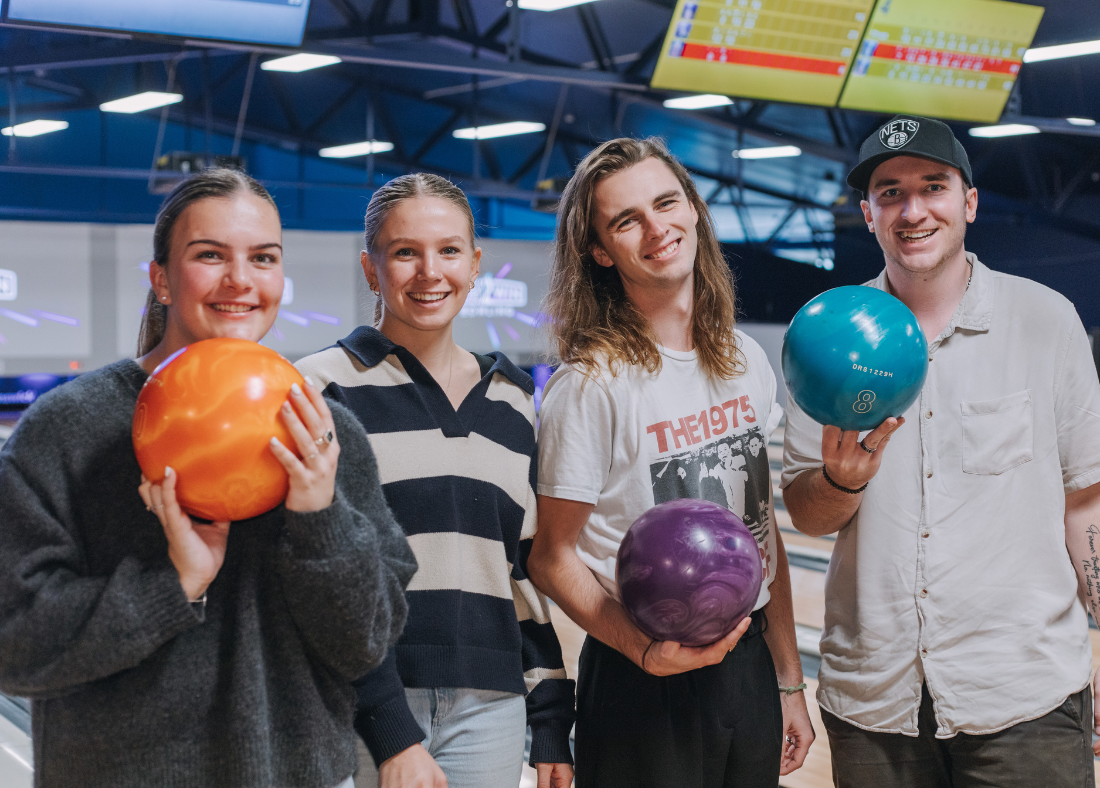 Two women and two men at Play2Win Bowling holding bowling balls and smiling with bowling alley in background
