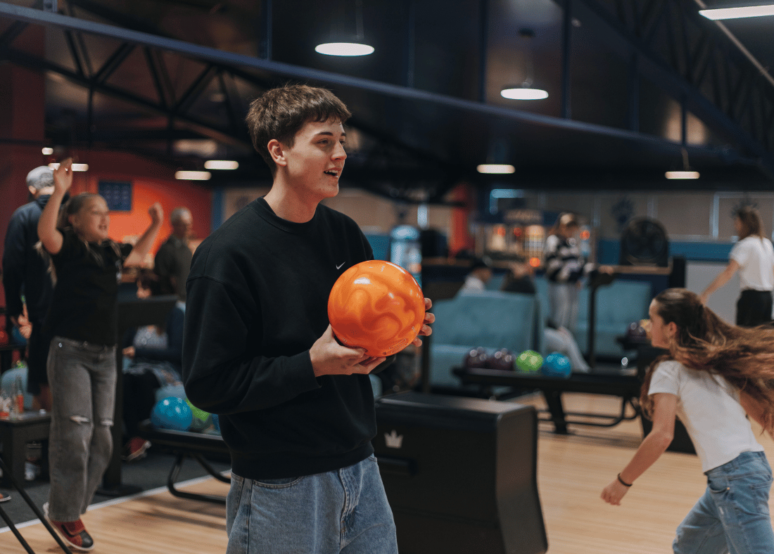 Person is bowling at Play2Win Bowling with teenagers in the background cheering on their friend