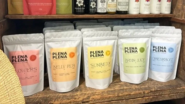 Pouches of herbal remedies or supplements labeled with different names and flavors on a wooden shelf.