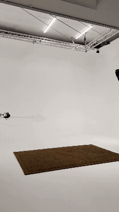 Empty photography studio with a brown rug on a white floor and ceiling-mounted lighting fixtures.