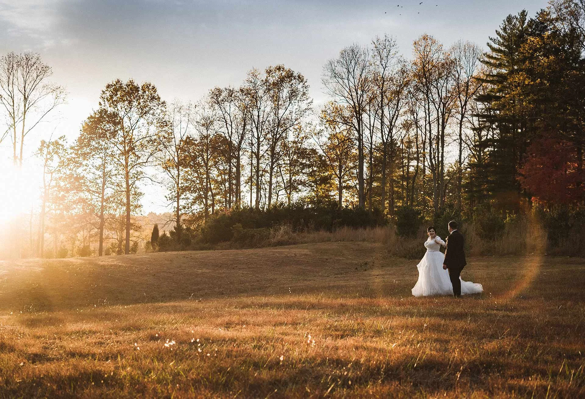 bride-leading-groom-through-a-field-during-sunset.jpg