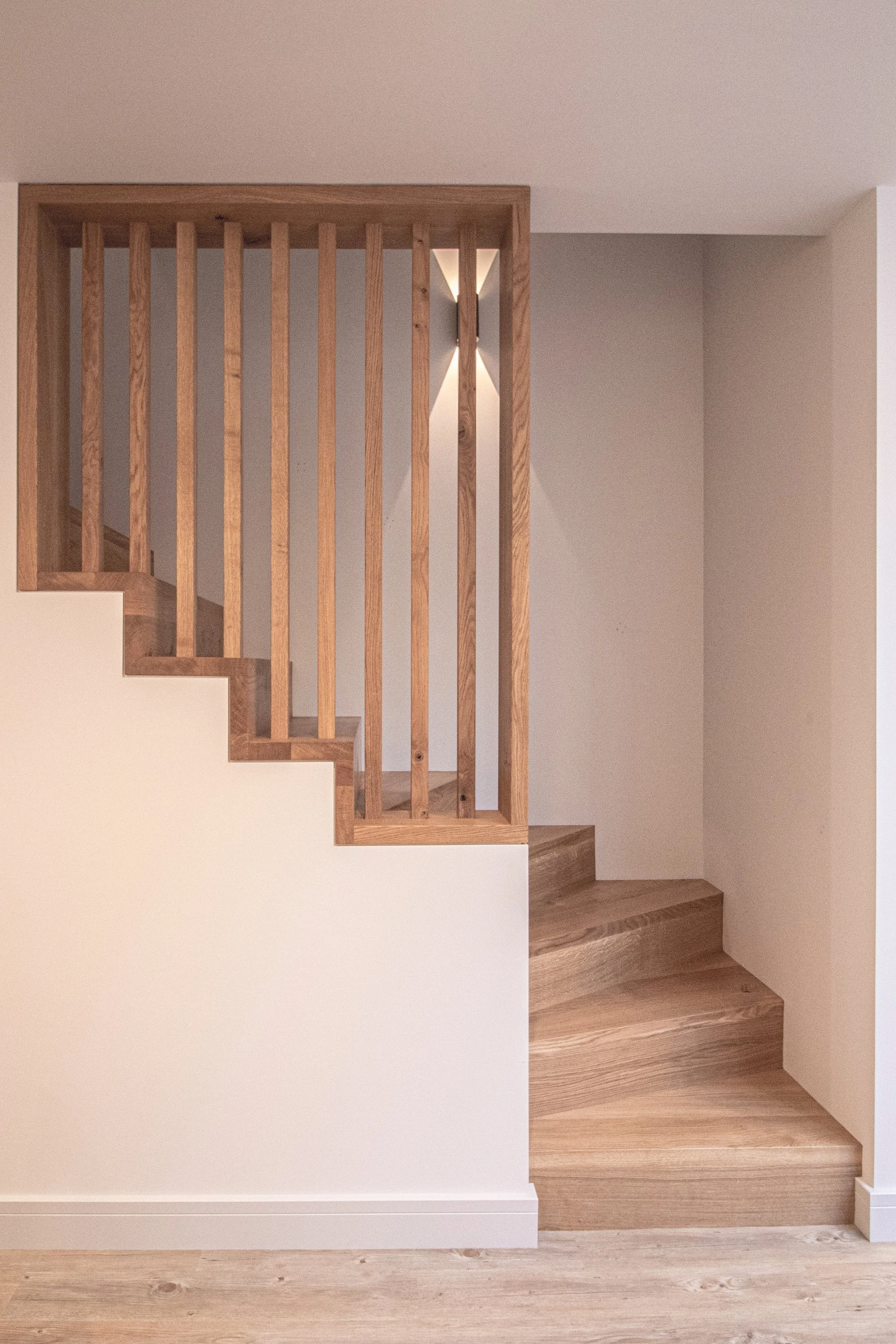 Bespoke wooden staircase with a railing, beige wall, and hardwood flooring.