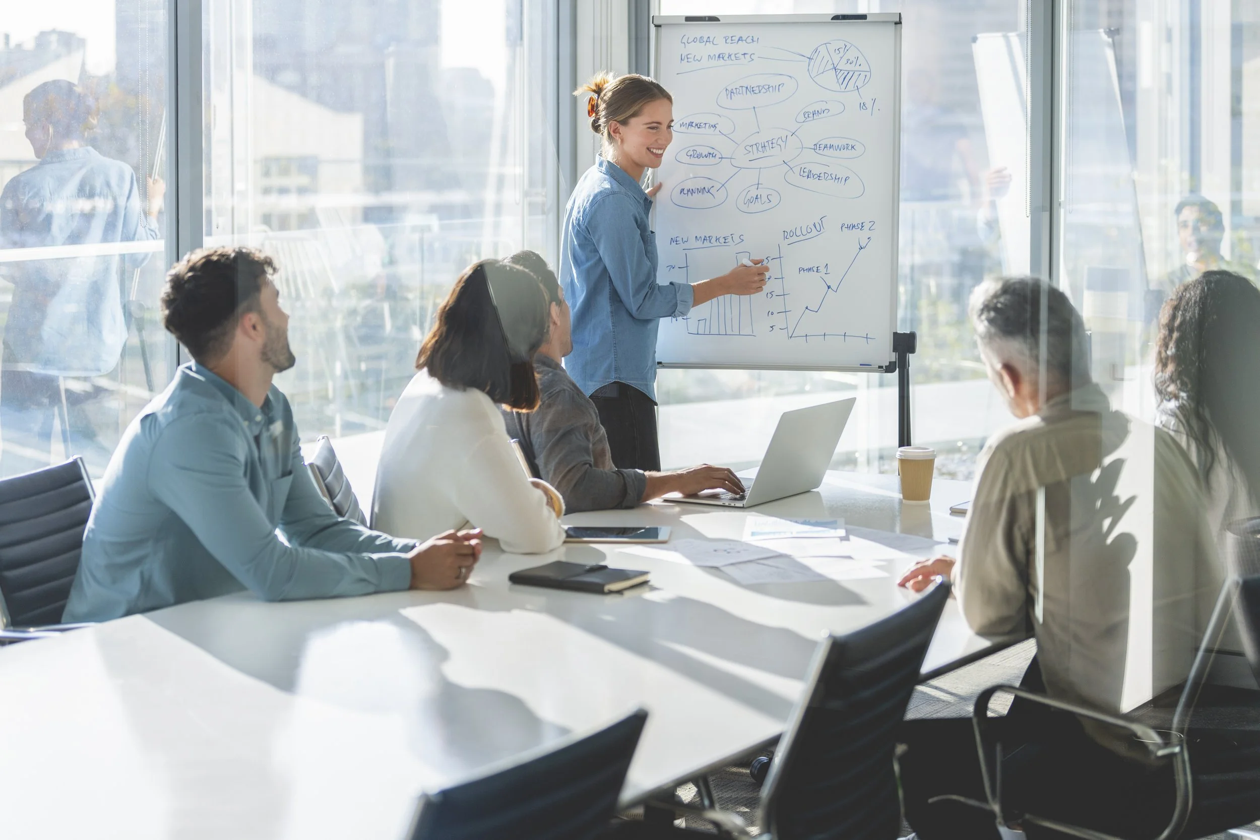 femme donnant une formation à un groupe de personne à l'aide d'un tableau blanc