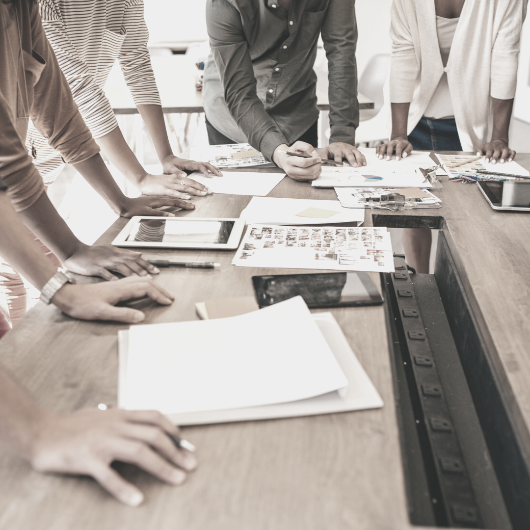 People gathered around a table reviewing documents, charts, and electronic devices in a professional meeting.