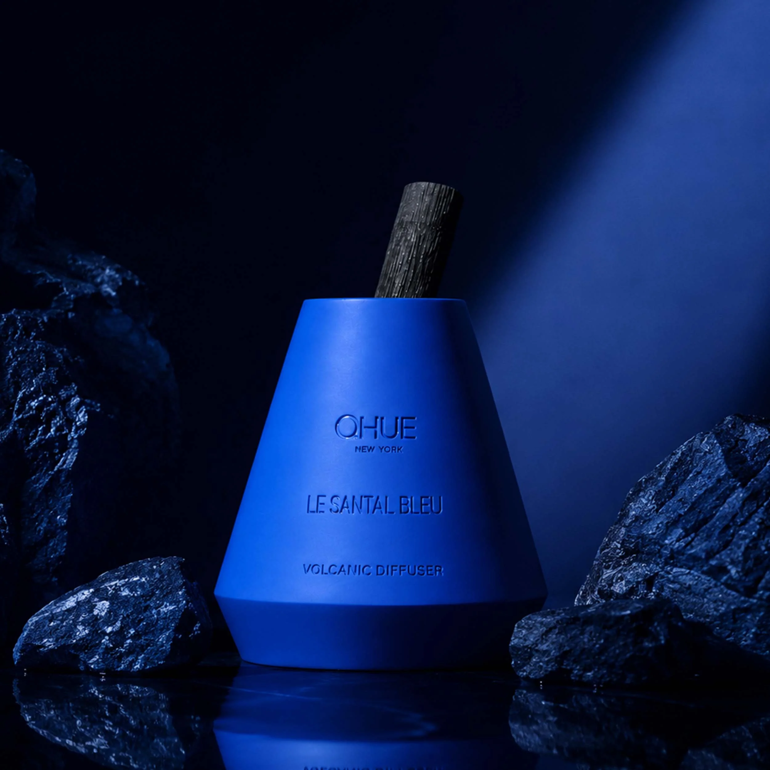 Qhue New York Le Santal Bleu Volcanic Reed Diffuser displayed among dark stone elements in a deep blue architectural setting.