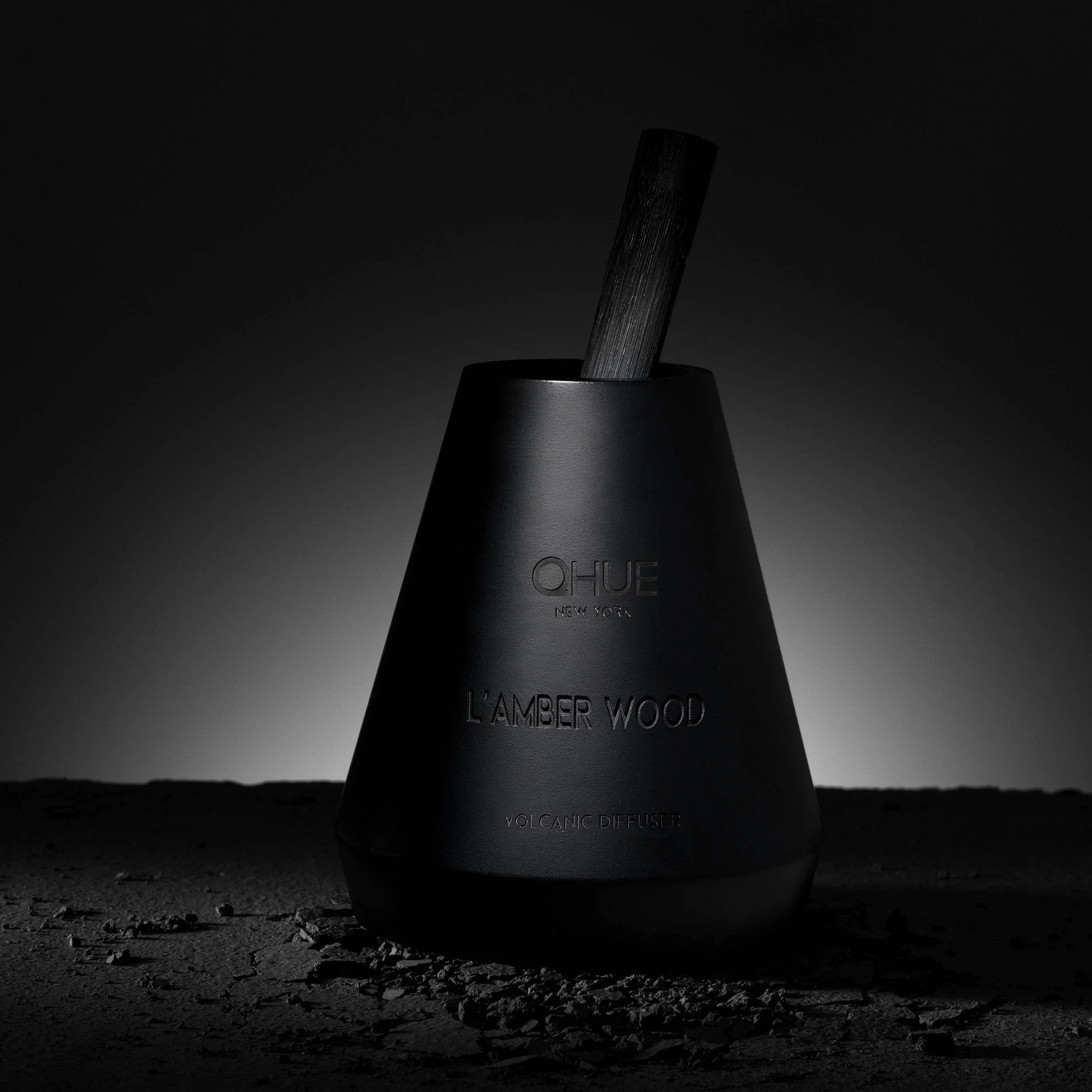 Qhue New York L’Amber Wood Volcanic Reed Diffuser in a dark luxury setting.